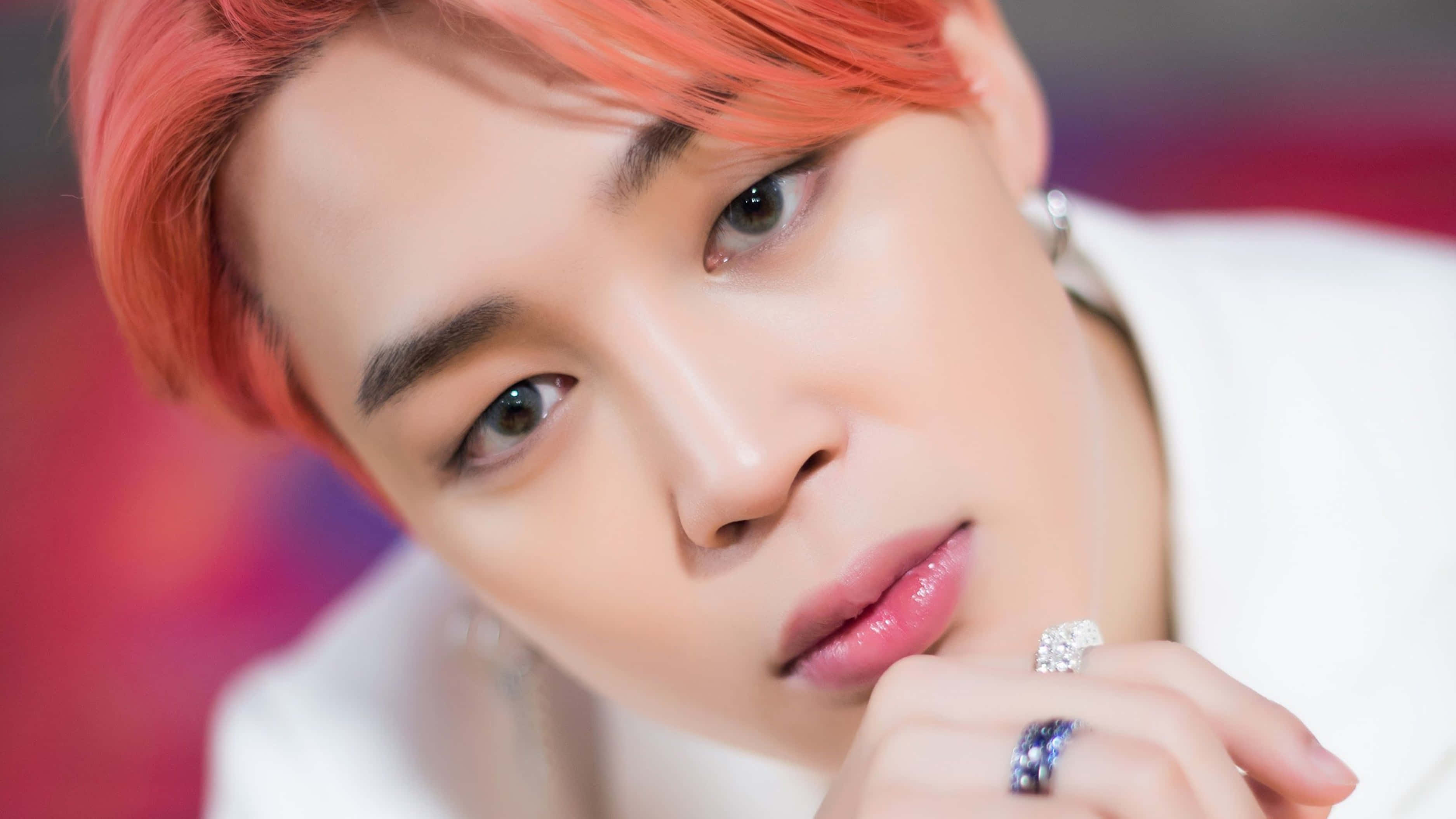 Bts Jimin 桌布 壁紙 — 近距離人像，人物擁有充滿活力的珊瑚色頭髮和鑽石戒指，背景為模糊的紅色。