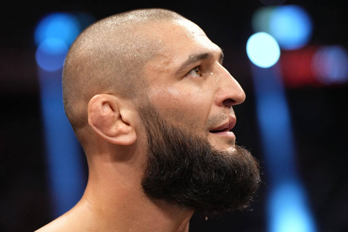 UFC 桌布 壁紙 — 近距離側面特寫，一名留鬚戰士在模糊藍色競技場燈光下，眼神凌厲。