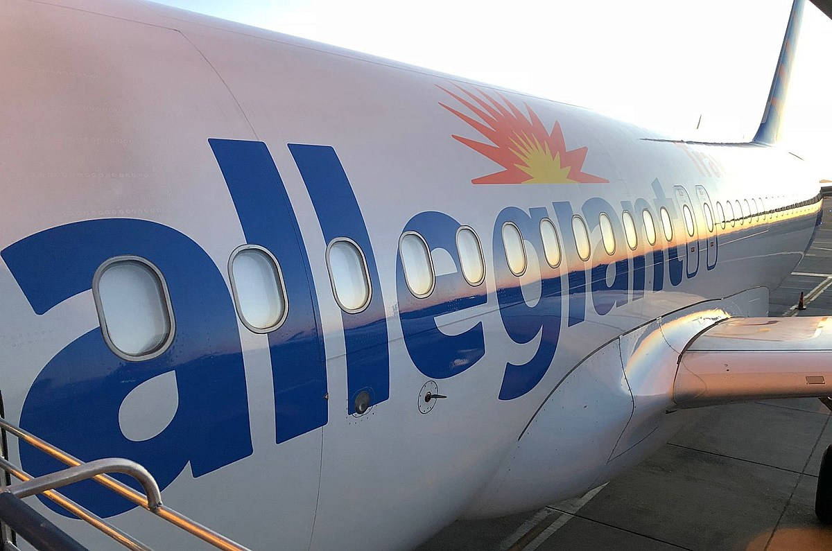 transportation 桌布 壁紙 — 近距離拍攝 Allegiant Air 客機機身，帶有藍色標誌和橙色太陽爆發設計，停機坪上。