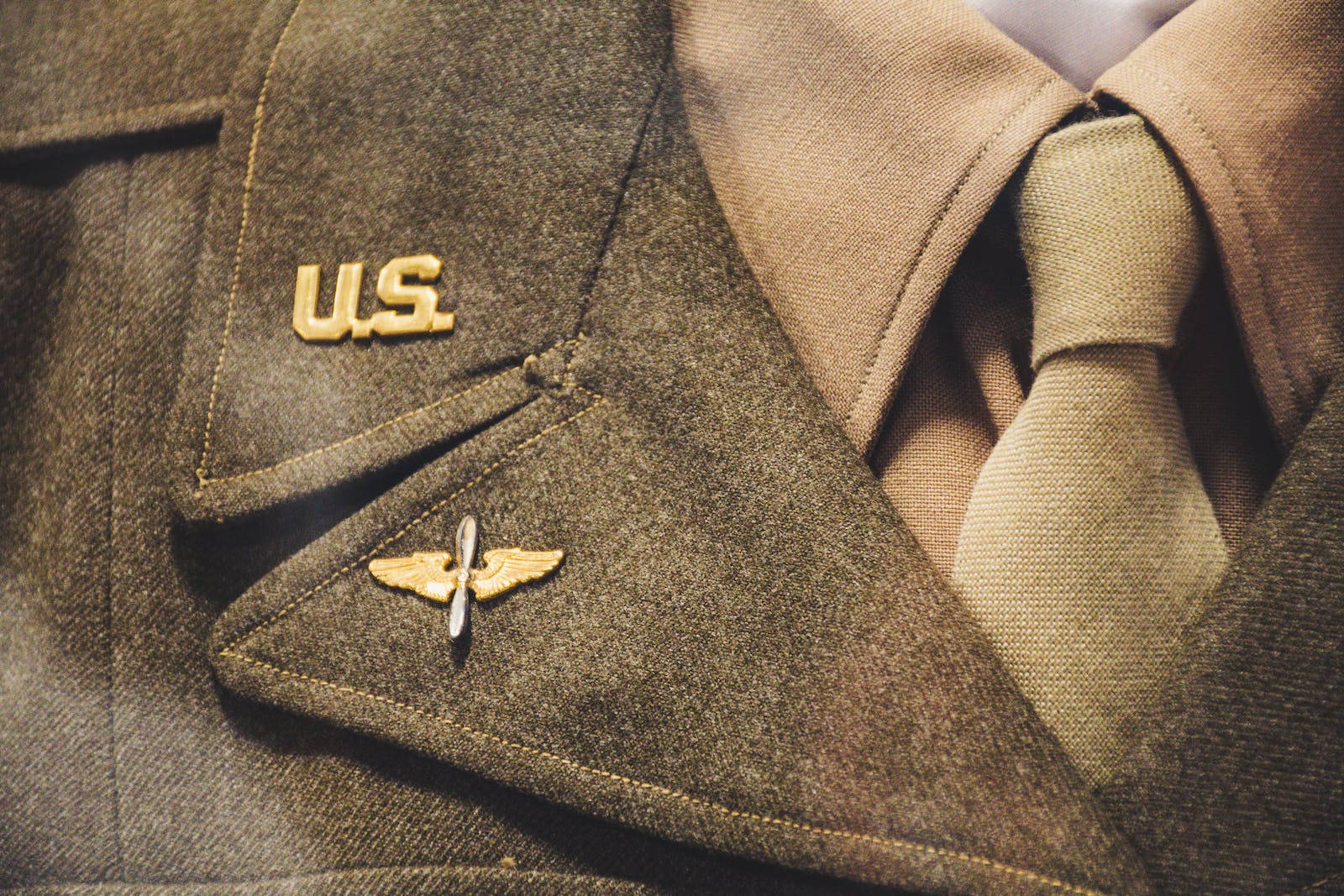 Air Force 桌布 壁紙 — 近距離拍攝一件復古美國軍裝外套，帶有金色翅膀和 'U.S.' 徽章，布料為質感橄欖色。