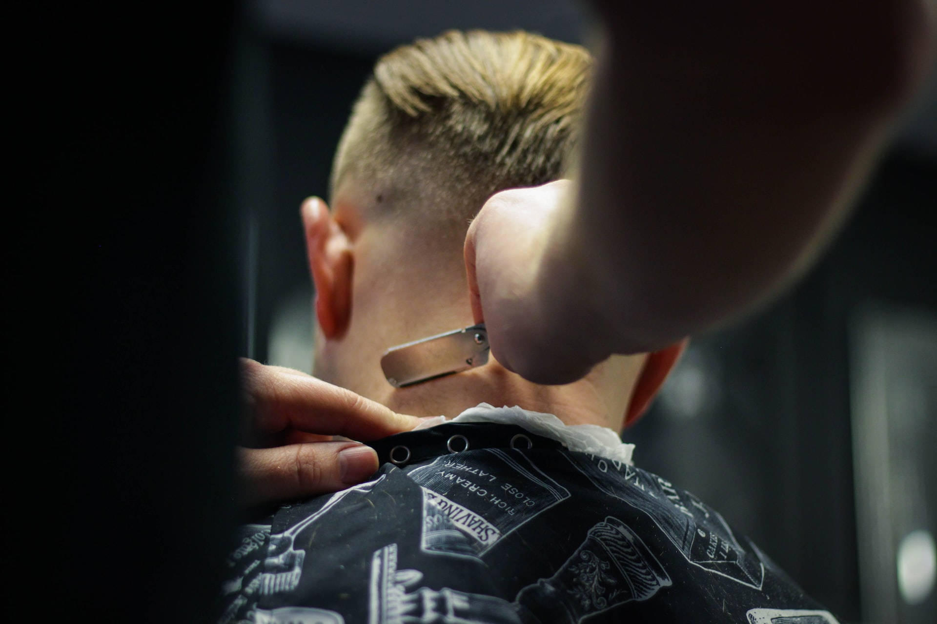 Haircut 桌布 壁紙 — 近距離拍攝一位理髮師在昏暗的理髮店裡，用直剃刀修剪男士頸部毛髮。