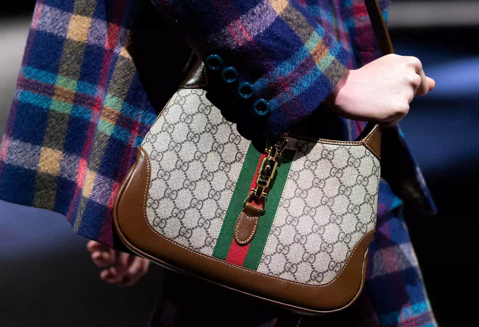 Gucci 桌布 壁紙 — 近距離拍攝一個人在戲劇性的天橋燈光下手持帶有GG字母組合和綠色紅色條紋的Gucci手提包。