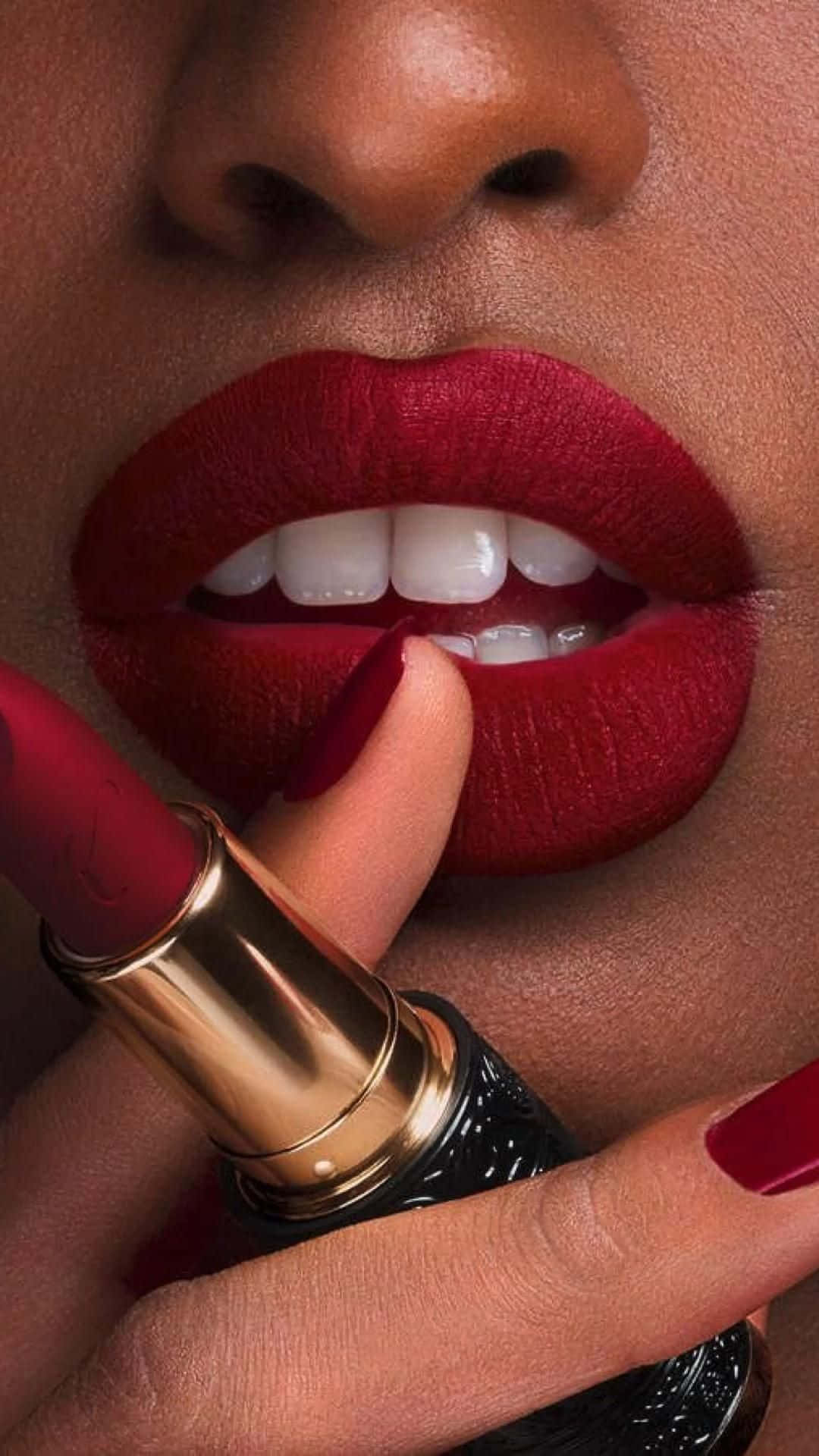 lipstick 桌布 壁紙 — 近距離拍攝一個人塗抹大膽紅色唇膏，搭配相配的美甲和閃亮金色管身。