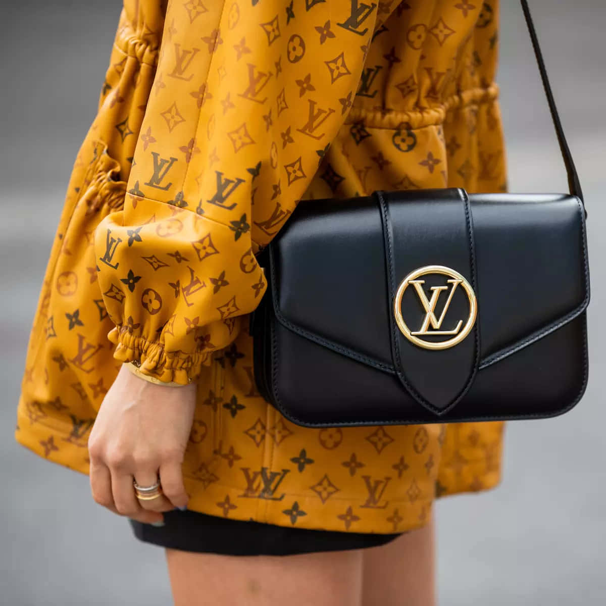 路易威登 桌布 壁紙 — 近距離拍攝一個人穿著芥末黃色 Louis Vuitton 字母組合外套，並攜帶一個帶有金色標誌的黑色 LV 手袋。