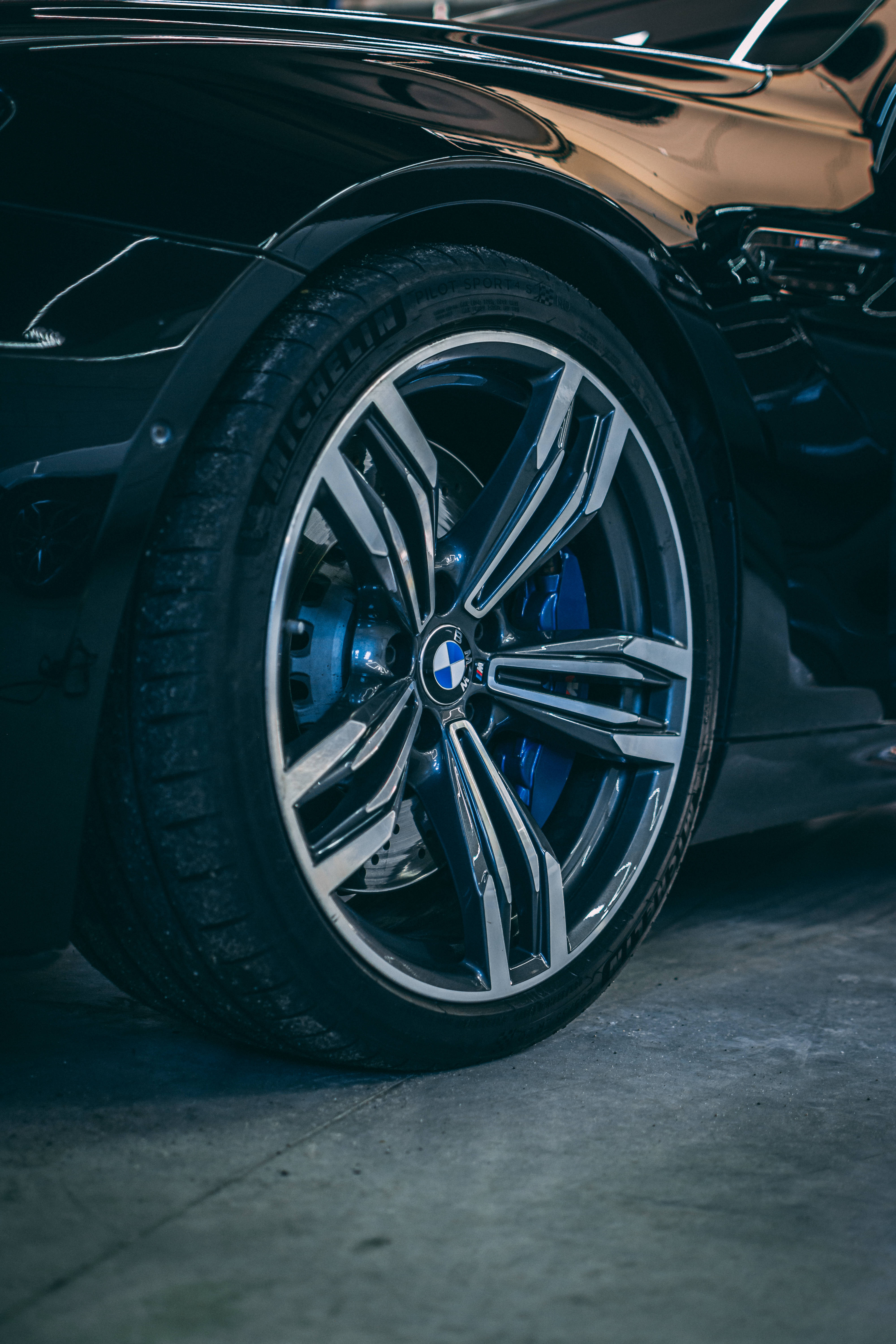 Black Bmw 桌布 壁紙 — 近距離拍攝一個時尚的黑色BMW汽車輪圈，配有藍色制動卡鉗和閃亮的鍍鉻輪輞，在戲劇性燈光下。
