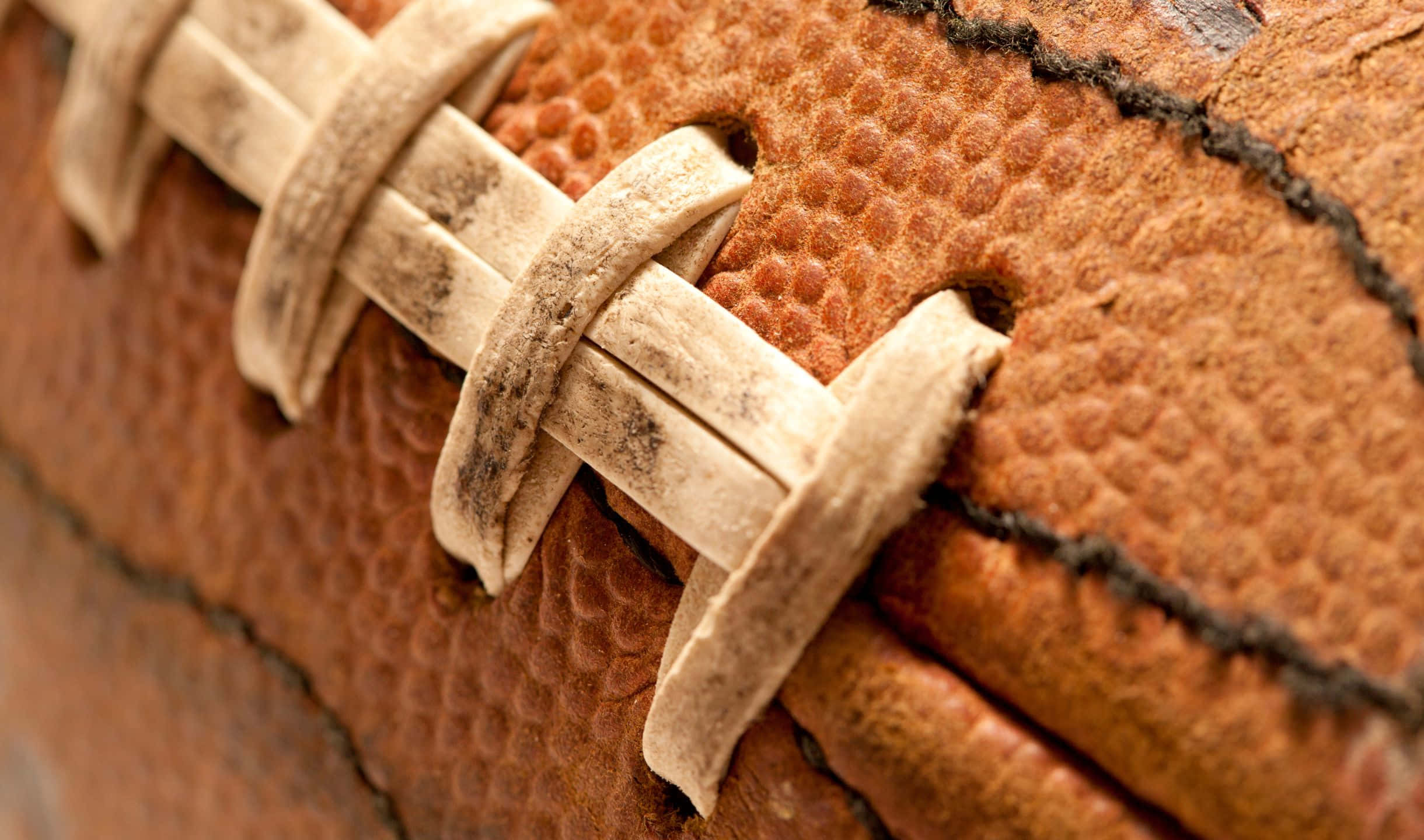 2440x1440 Football 桌布 壁紙 — 近距離拍攝一個磨損嚴重的棕色皮革足球，顯示出紋理表面和磨損的鞋帶。