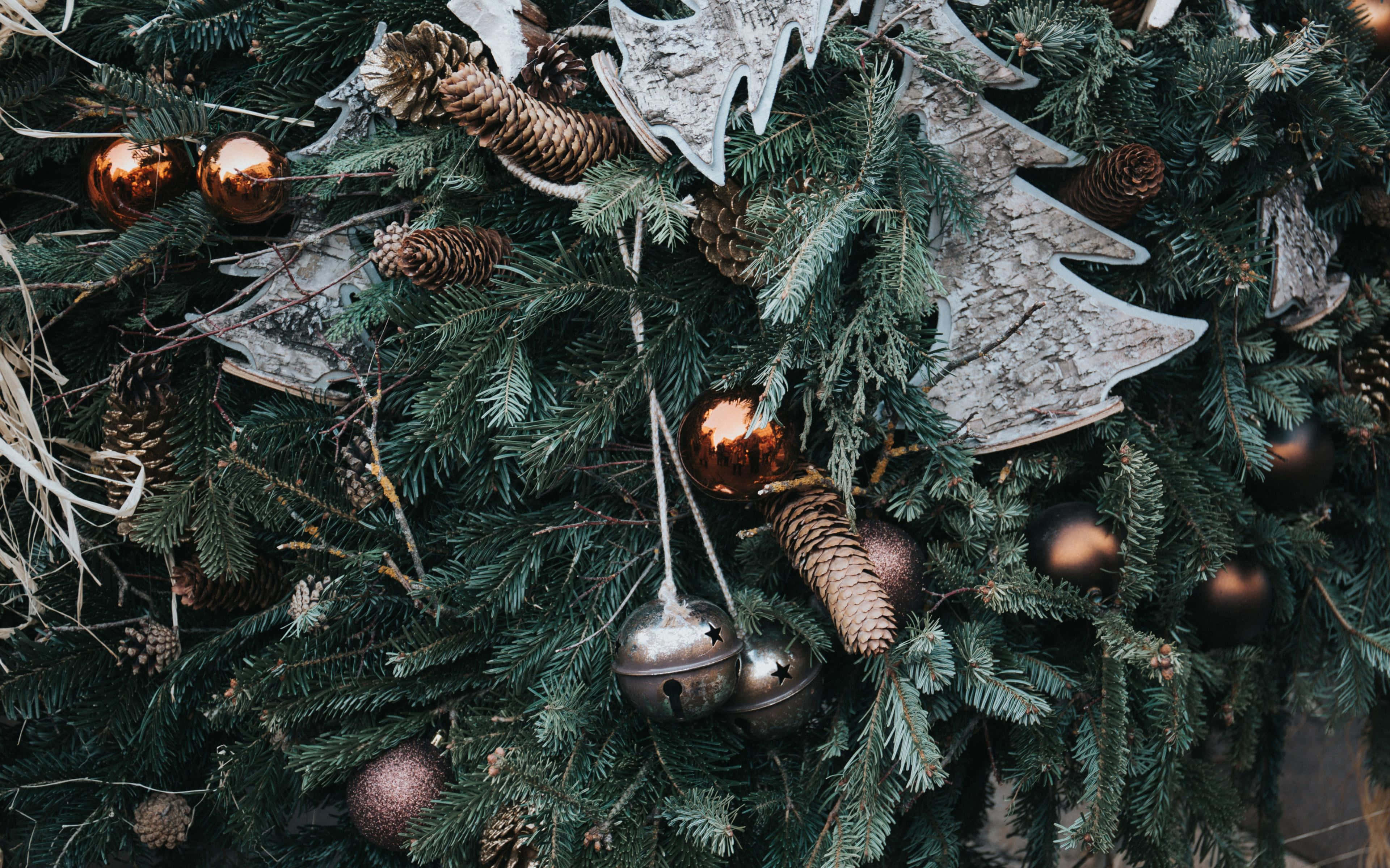 Rustic Christmas 桌布 壁紙 — 近距離拍攝一個茂密的綠色冷杉花環，裝飾著松果、金屬鈴鐺和質樸的木製樹形剪影。
