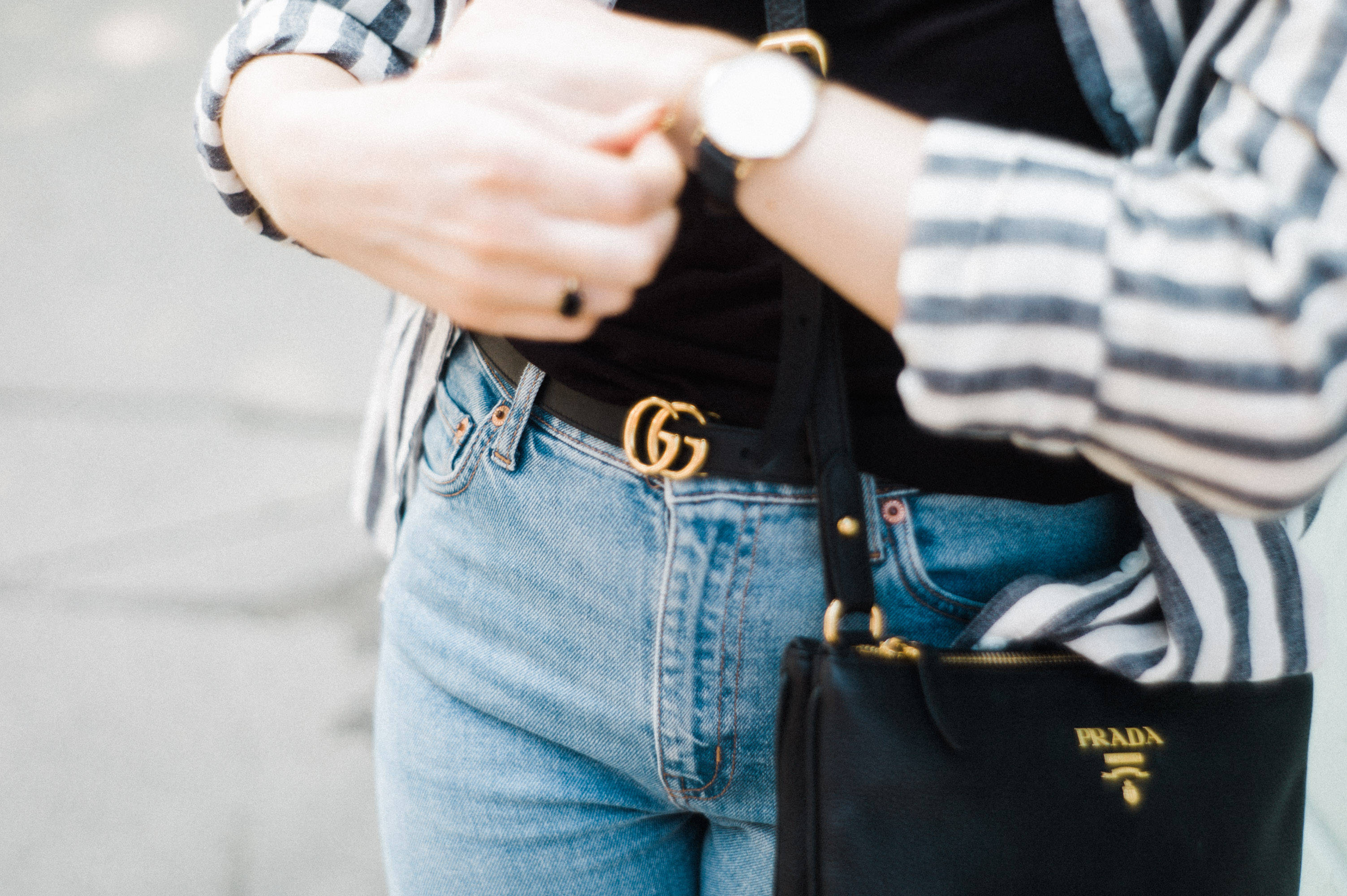 Prada 桌布 壁紙 — 近距離拍攝一名穿著條紋襯衫和牛仔褲的人，正在查看手錶，並配有Prada手袋和Gucci皮帶。