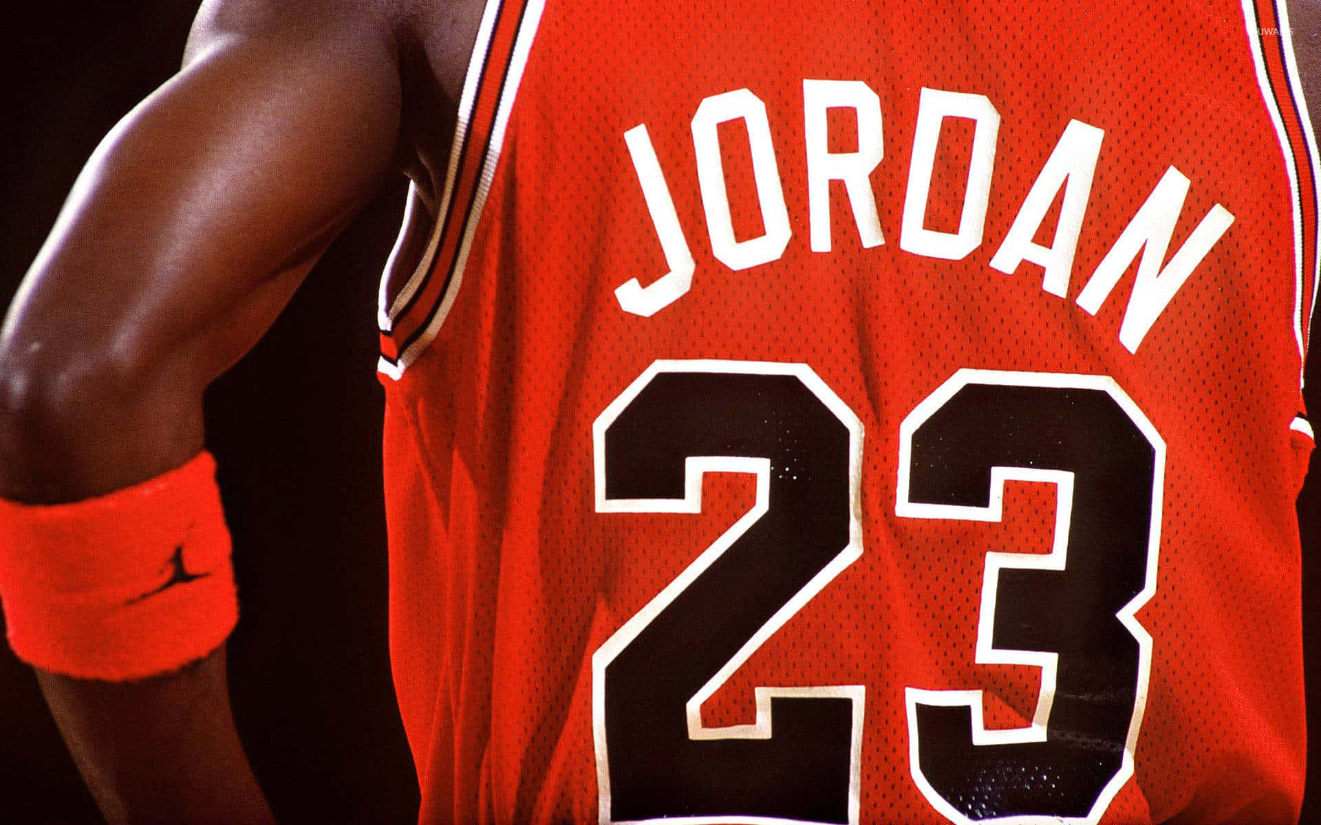 桌布 壁紙 — 近距離拍攝一名籃球運動員穿著紅色Jordan 23球衣，配以相配的腕帶，背景為深色。