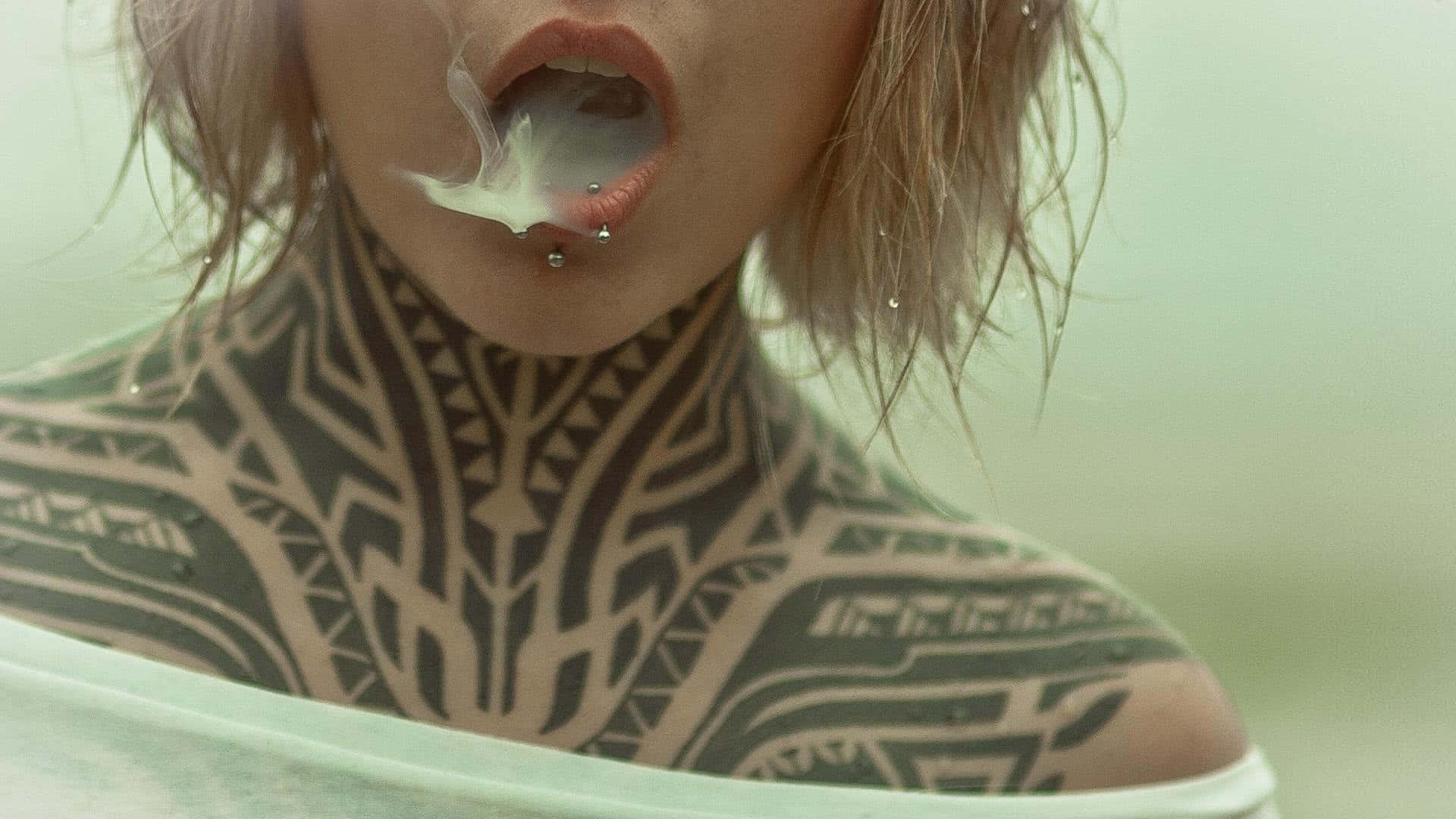 Tattoo 桌布 壁紙 — 近距離拍攝一名頸部和肩部有複雜黑色部落紋身的人，從口中呼出煙霧，並有唇環。