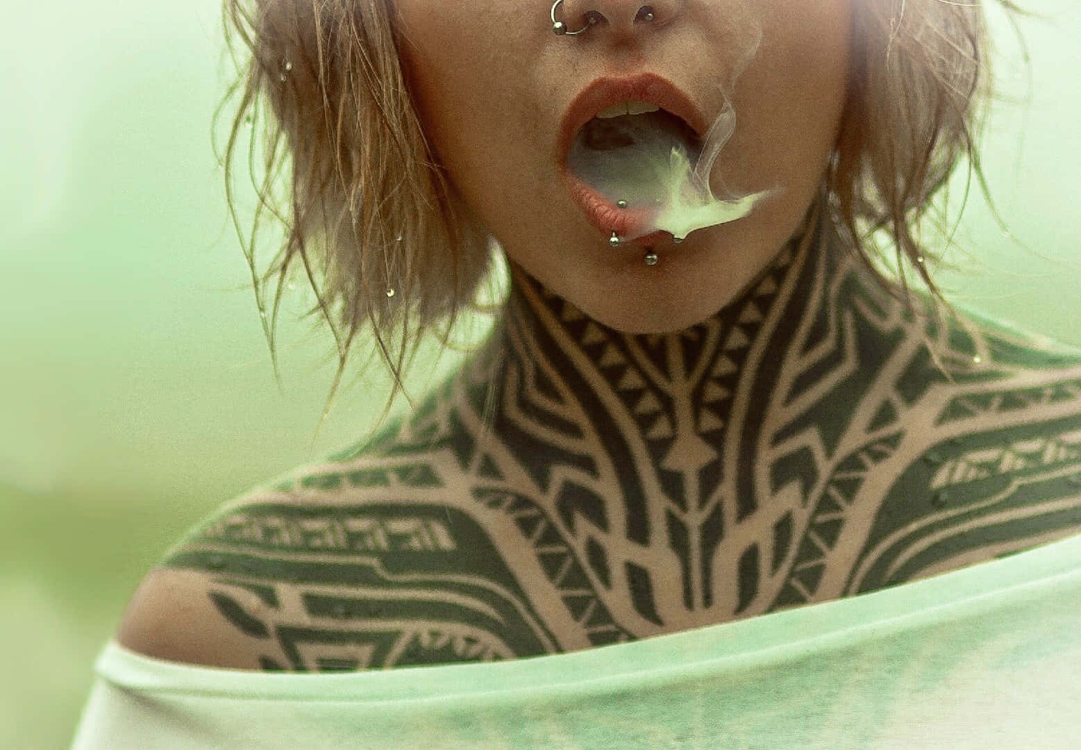 Tattoo 桌布 壁紙 — 近距離拍攝一名頸部有複雜刺青的人，穿著淺綠色上衣呼出煙霧。