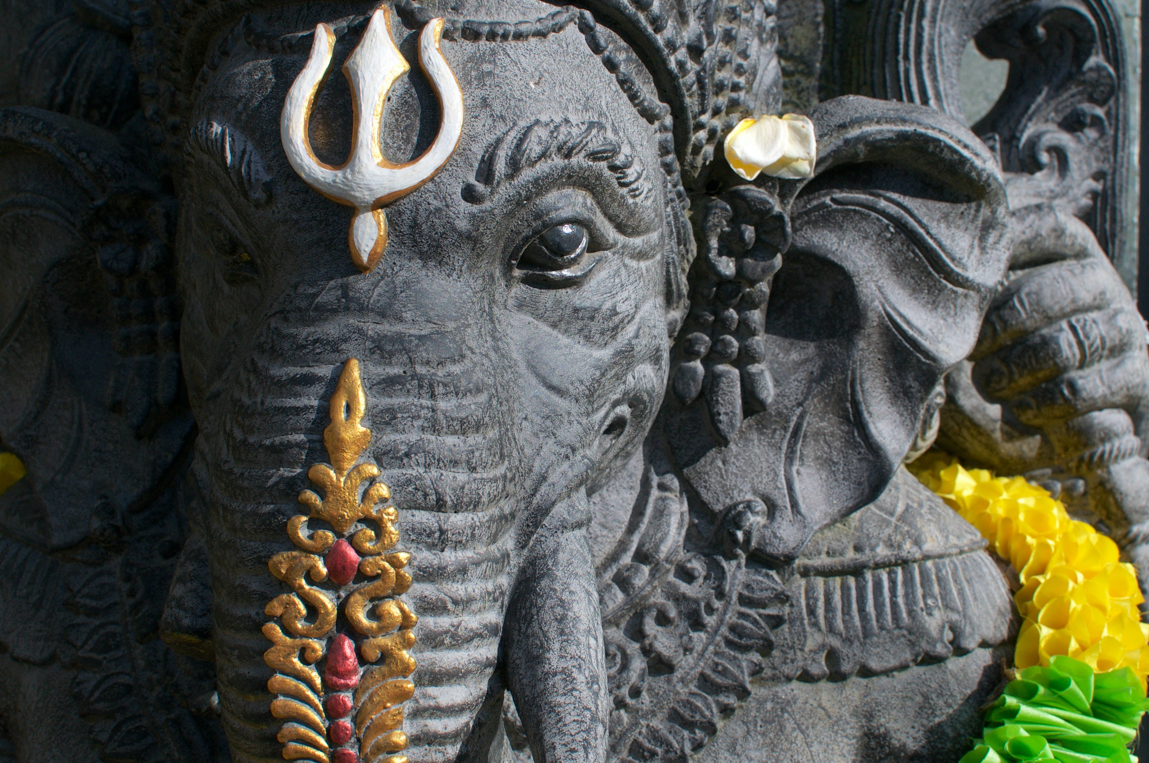 ganesh 4K 桌布 壁紙 — 近距離拍攝一尊細節豐富的象神石像，在明亮陽光下飾有金色和黃色花環。