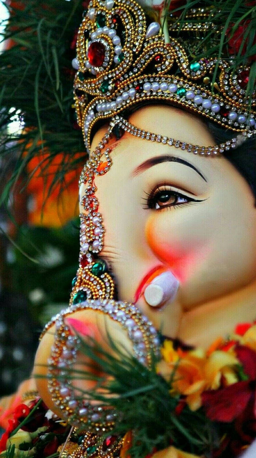 hindu iPhone 桌布 壁紙 — 近距離拍攝一尊裝飾華麗的象神像，戴有寶石皇冠和花環，背景是模糊的綠色。