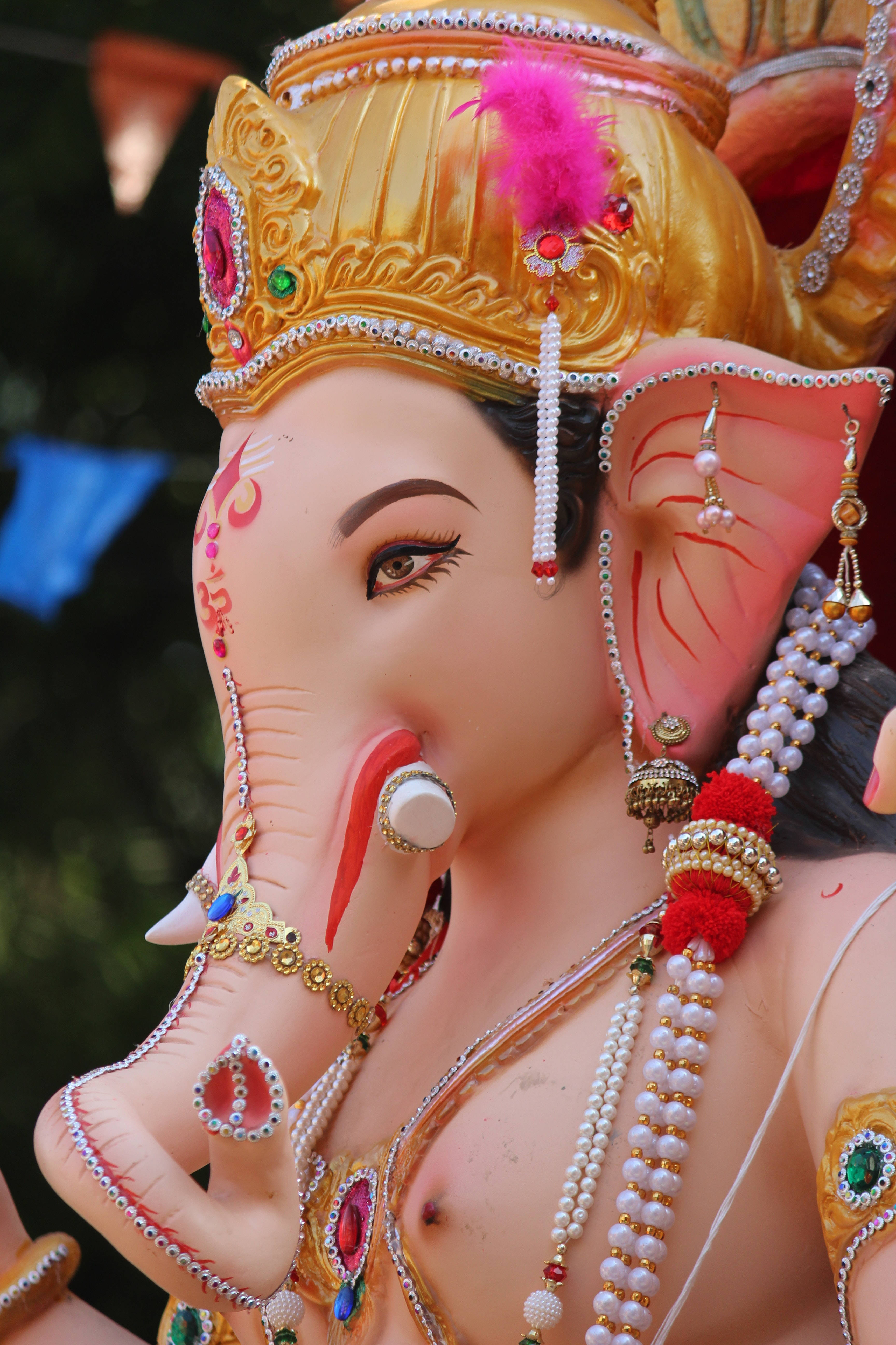 ganesh iPhone 桌布 壁紙 — 近距離拍攝一尊裝飾鮮豔的象頭神像，飾有金色珠寶、粉紅色羽毛和珍珠項鍊。