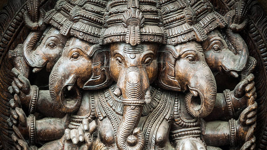 Hindu God 桌布 壁紙 — 近距離拍攝一尊雕刻精細的象頭神青銅像，周圍環繞著多個象頭。