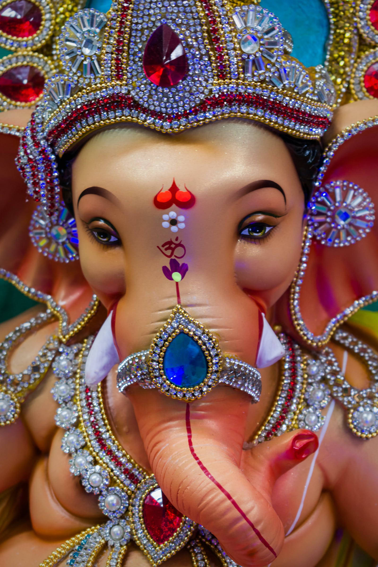 Vinayaka 桌布 壁紙 — 近距離拍攝一尊飾有豐富珠寶的象頭神像，帶有紅色眉心點和藍寶石鼻環。