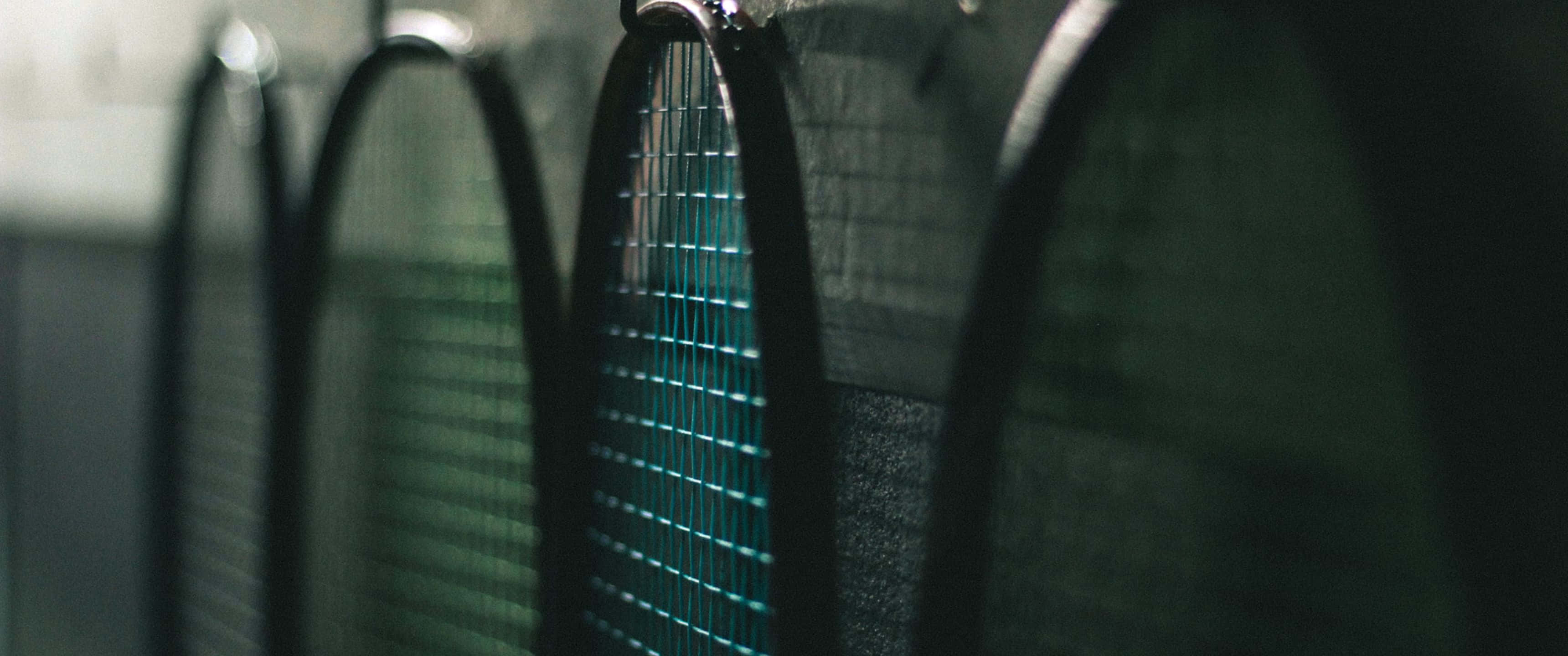3440x1440p Badminton 桌布 壁紙 — 近距離拍攝一排網球拍，置於昏暗房間中，帶有青綠色線條亮點。