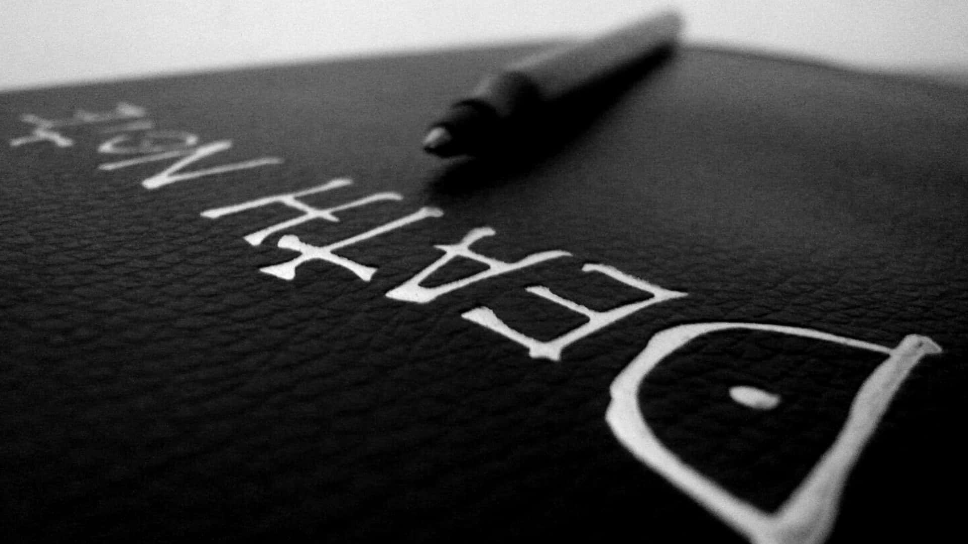 死亡筆記本 桌布 壁紙 — 近距離拍攝一本黑色皮面書，書名為「DEATH NOTE」，上面放著一支筆，單色調。