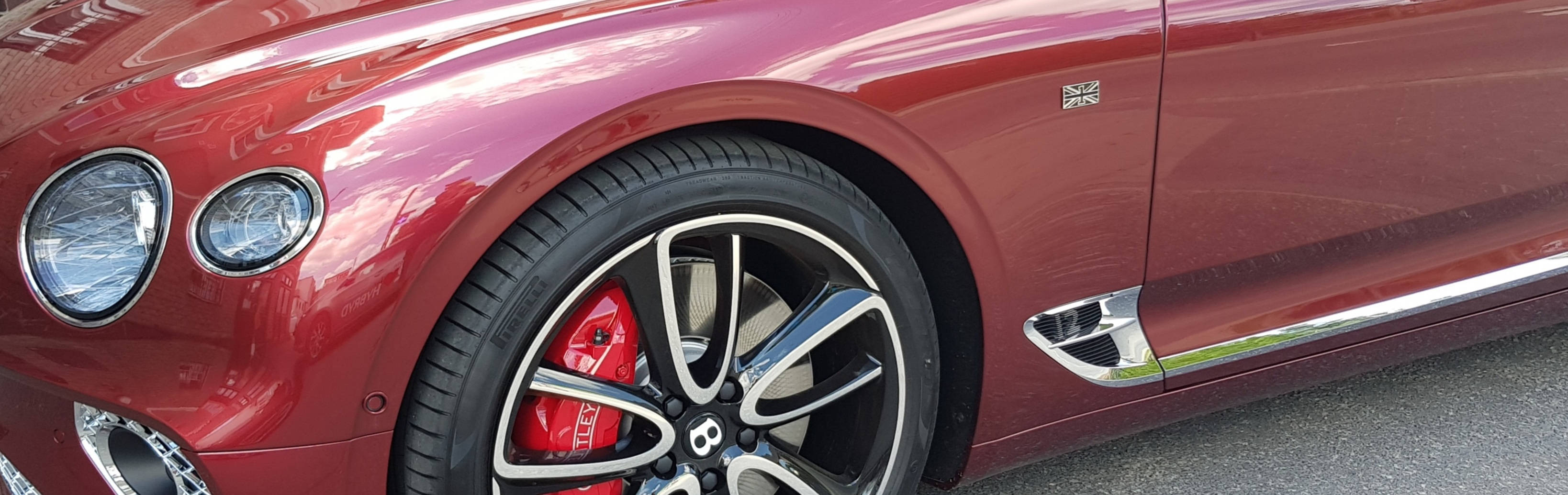 Bentley Cars 桌布 壁紙 — 近距離拍攝一輛光面紅色賓利，帶有鍍鉻裝飾和紅色制動卡鉗，位於鋪砌表面上。