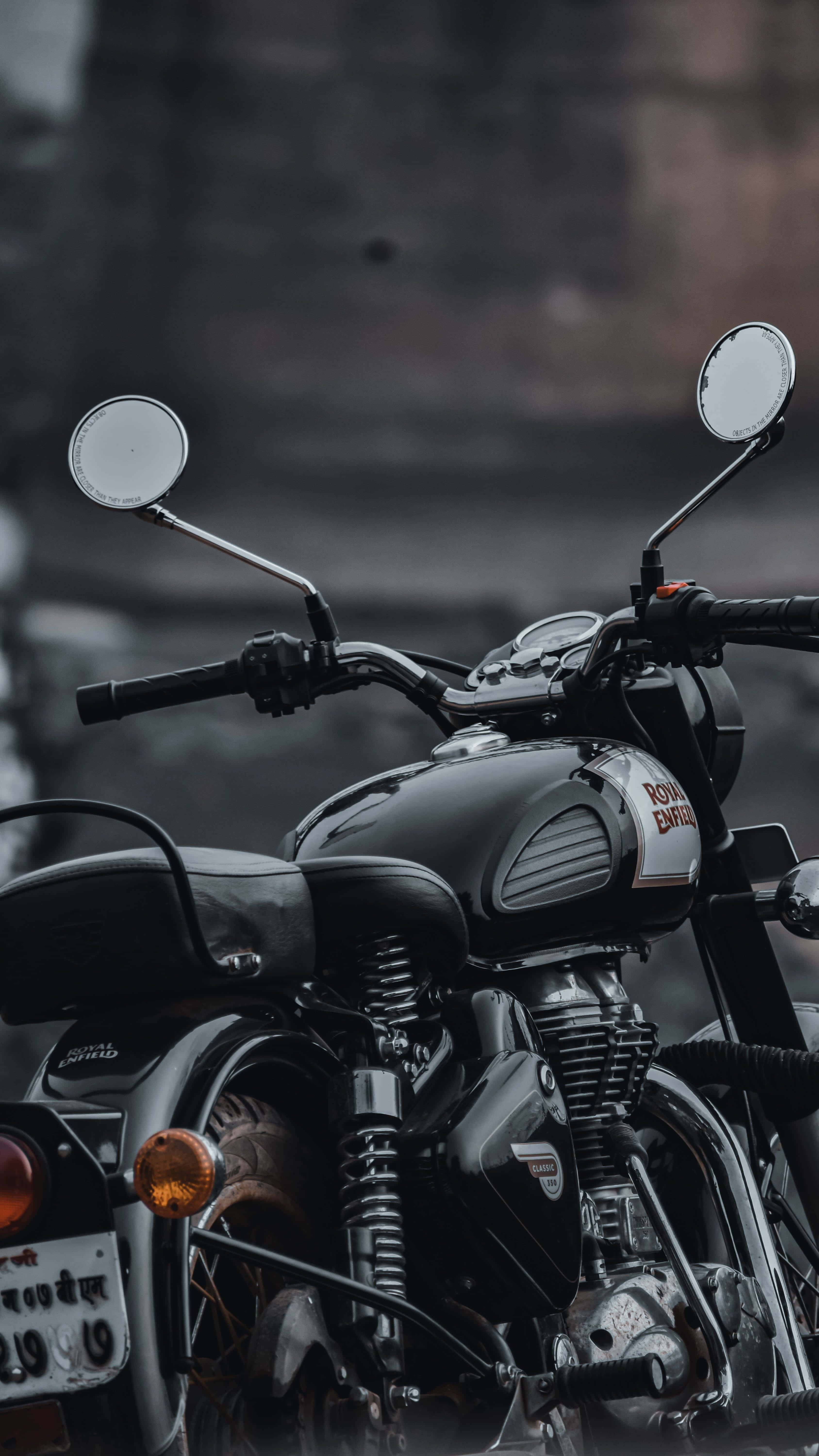 Royal Enfield Bullet 桌布 壁紙 — 近距離拍攝一輛時尚黑色 Royal Enfield 機車，帶有鍍鉻裝飾和圓形後視鏡，背景是模糊的城市景觀。