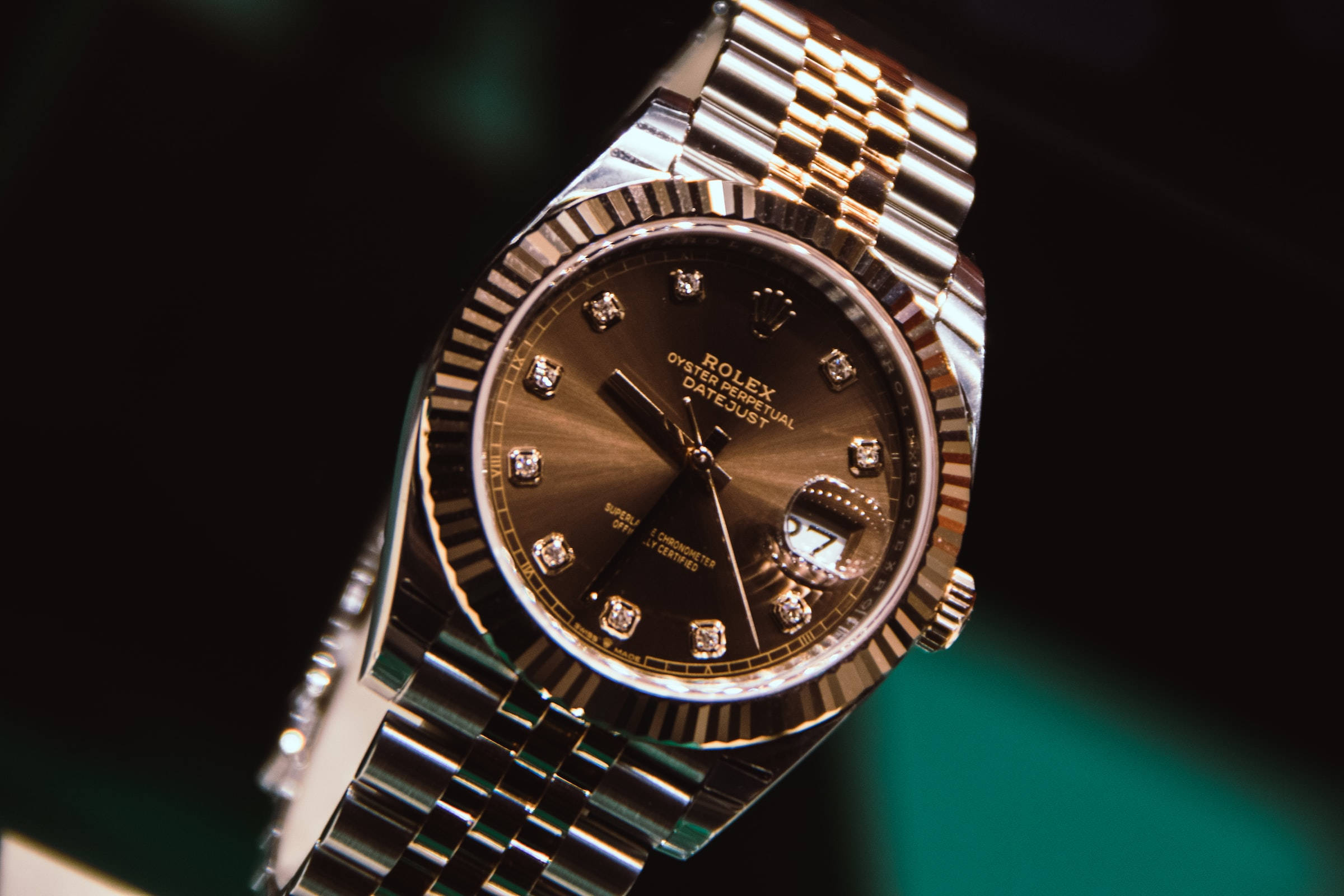 復古 桌布 壁紙 — 近距離拍攝一隻奢華的金色和鋼製勞力士 Oyster Perpetual Datejust 手錶，帶有鑽石小時標記，背景為深色。