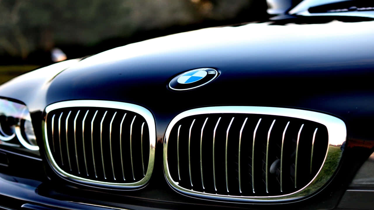 720p Bmw 桌布 壁紙 — 近距離拍攝亮黑色BMW引擎蓋，在柔和燈光下展示標誌性鍍鉻腎形格柵和圓形標誌。