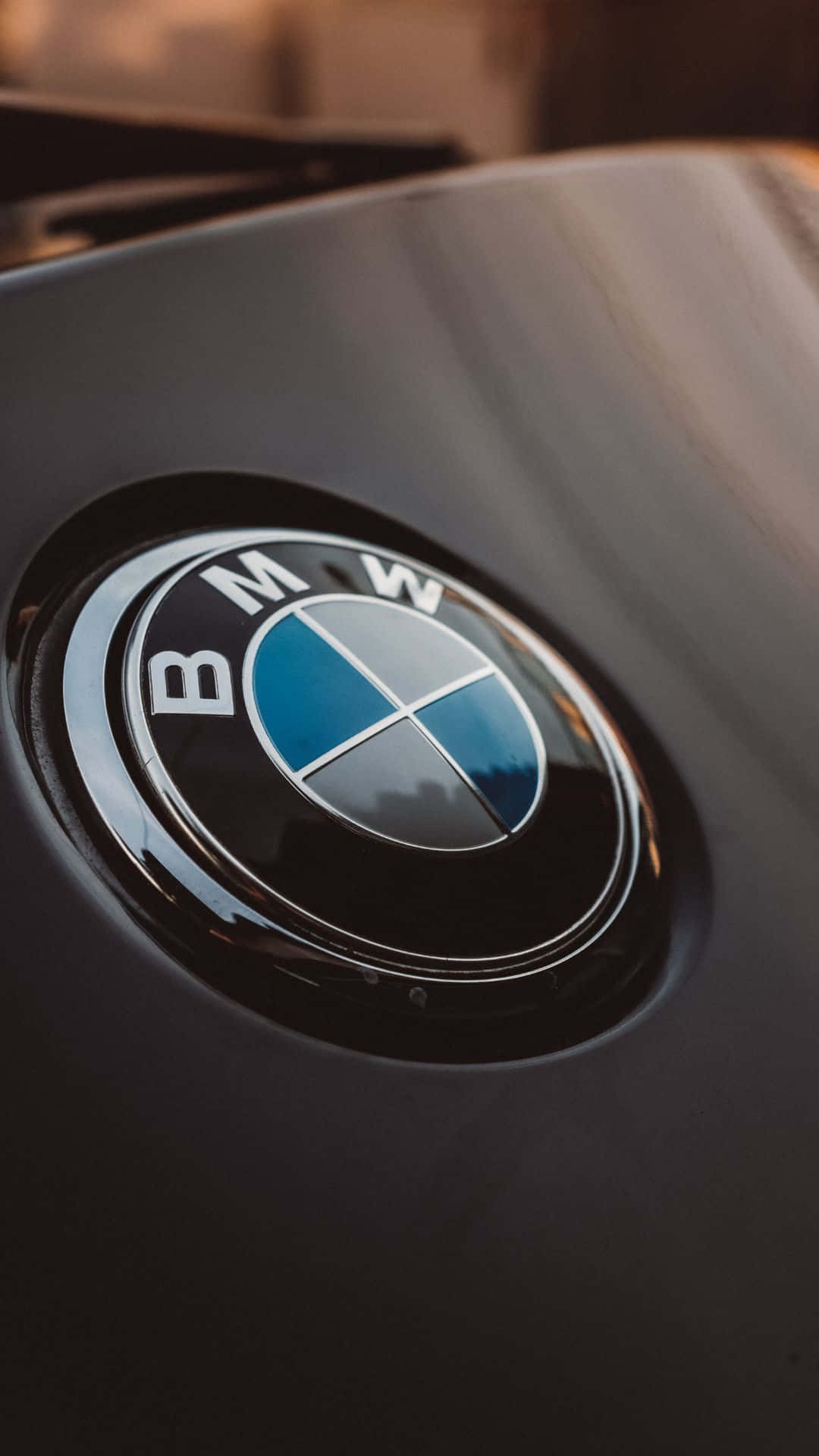 Android Bmw 桌布 壁紙 — 近距離拍攝亮黑色BMW標誌，在流線型引擎蓋上反射溫暖環境光。