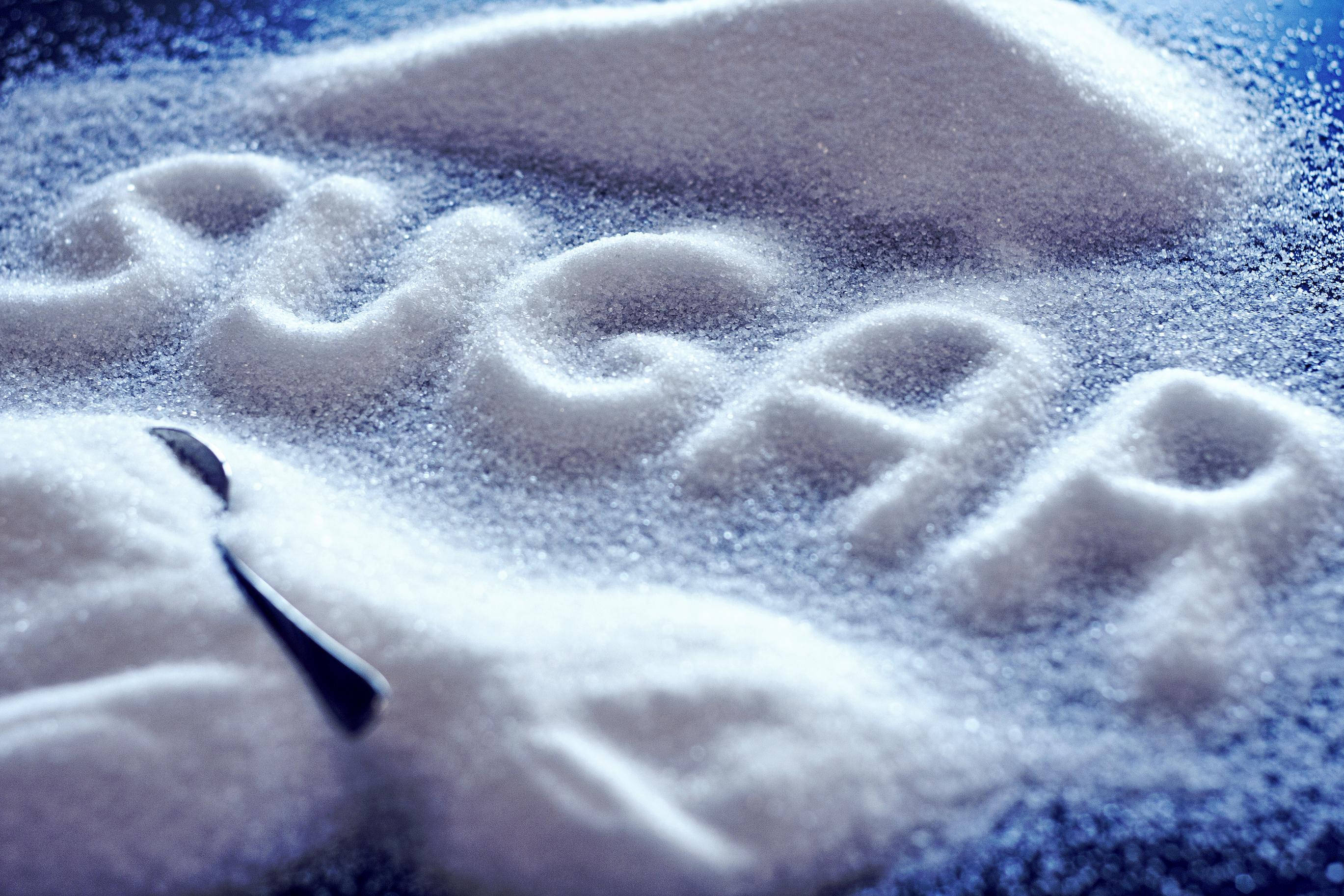 Sugar 桌布 壁紙 — 近距離拍攝以白砂糖拼出的「糖」字，旁邊放著一隻湯匙，在冷藍色燈光下。