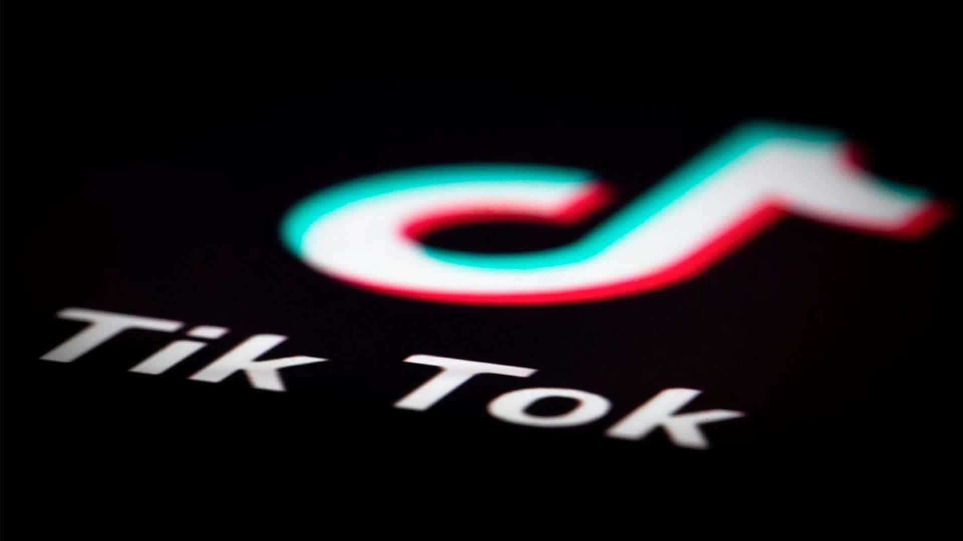 TikTok Logo 桌布 壁紙 — 近距離拍攝在深色背景上發出紅色、藍綠色和白色光芒的TikTok標誌。