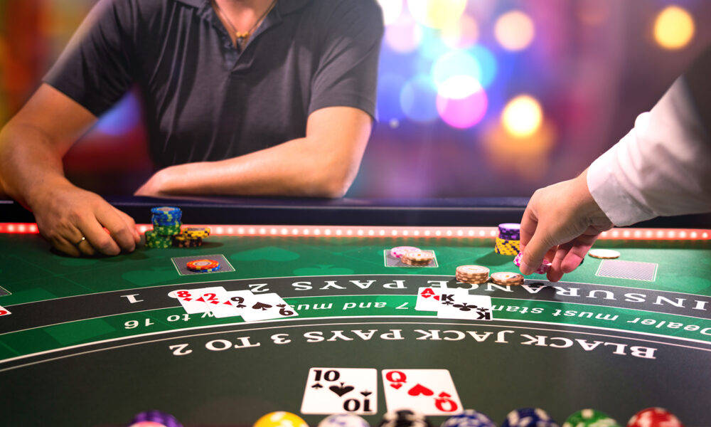 Casino 桌布 壁紙 — 近距離拍攝在賭場桌上玩二十一點的手部特寫，背景有彩色籌碼和閃爍燈光。