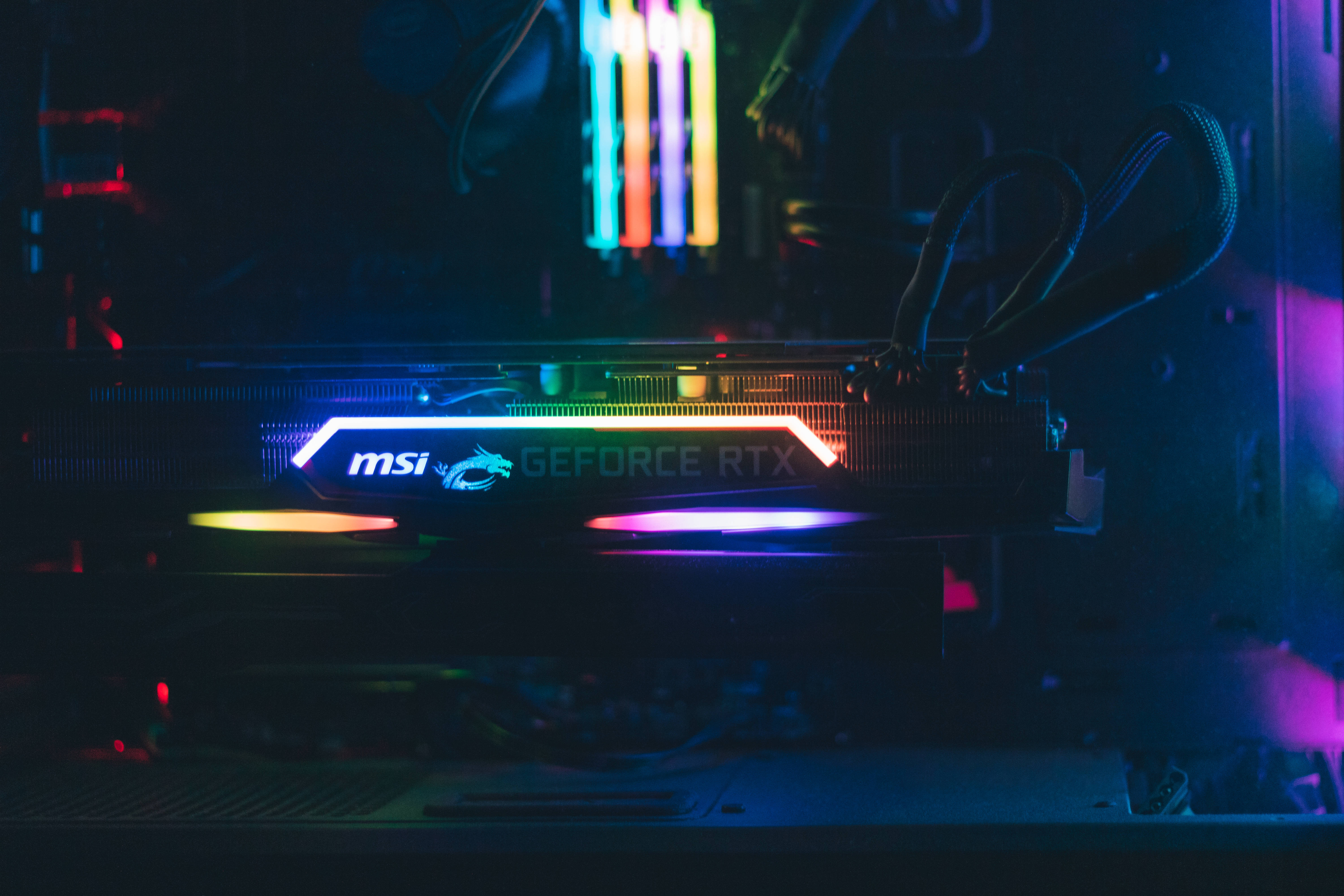 msi 2560x1080 桌布 壁紙 — 近距離拍攝在黑暗電腦機箱內閃爍著鮮豔RGB燈光的MSI GeForce RTX顯示卡。