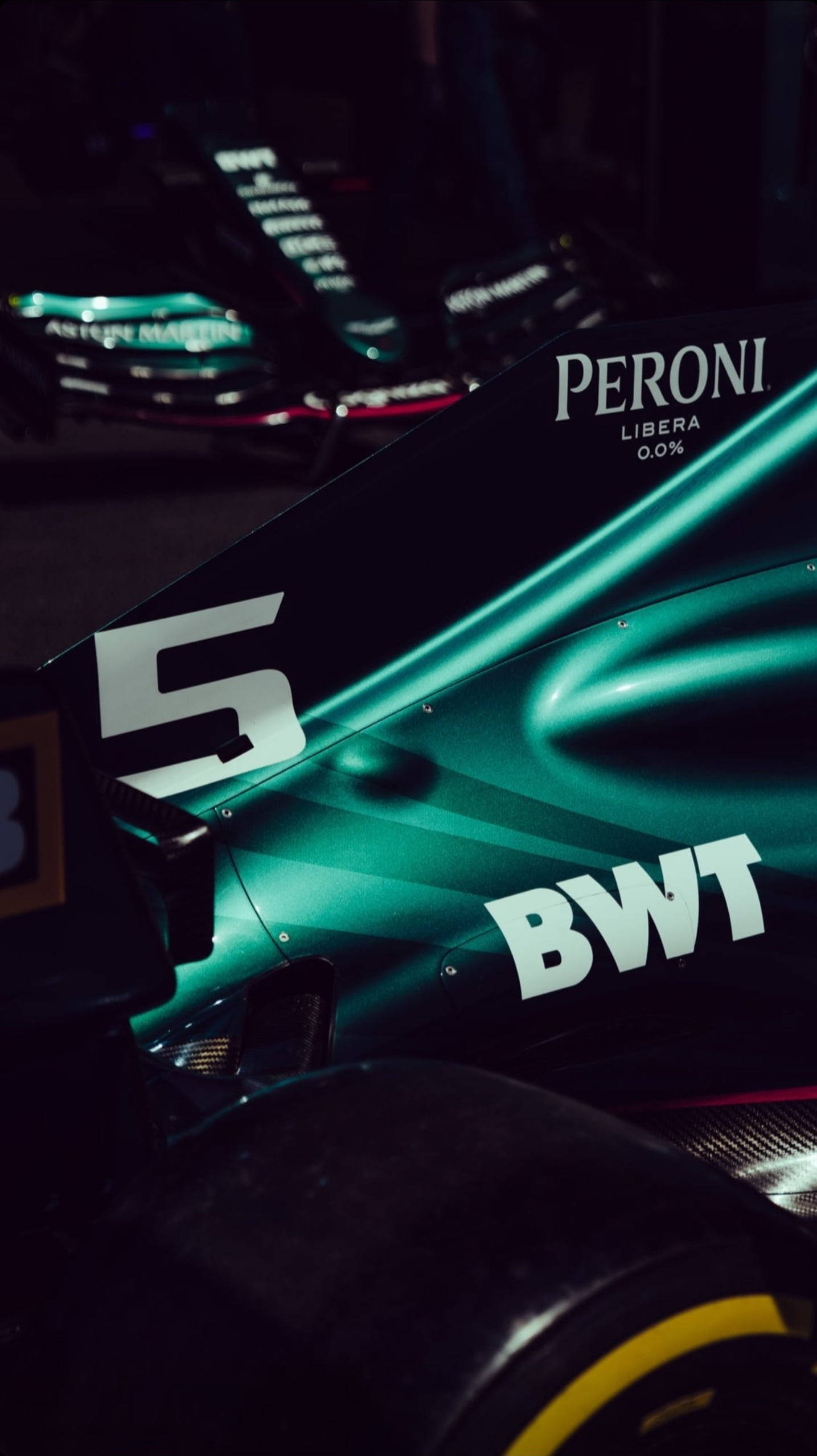 F1 iPhone 壁紙 桌布 壁紙 — 近距離拍攝時尚綠色賽車的後翼和輪胎，在戲劇性燈光下帶有贊助商標誌。