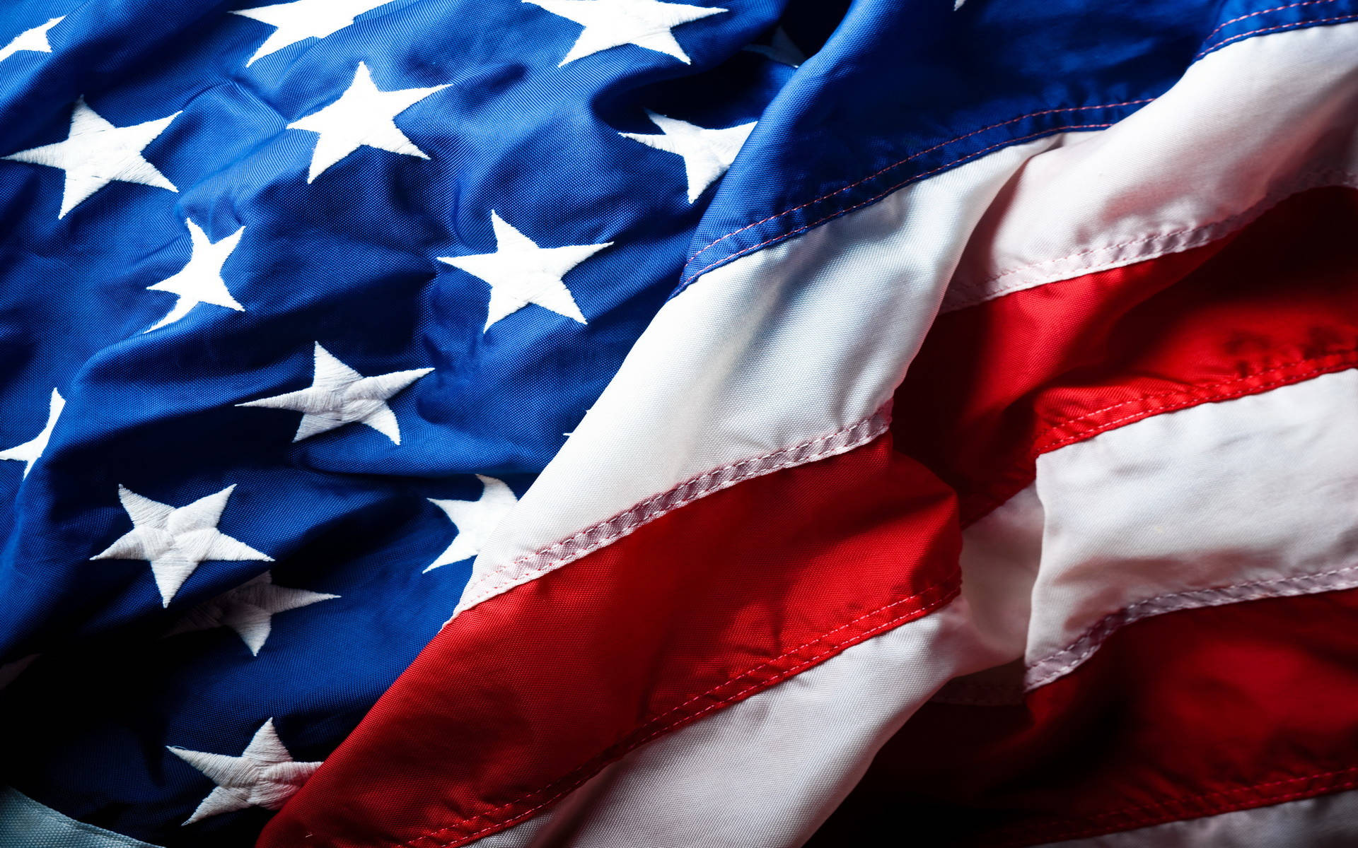 USA flag iPhone 桌布 壁紙 — 近距離拍攝有紋理的美國國旗，星星和條紋在戲劇性燈光下以柔軟的褶皺垂墜。