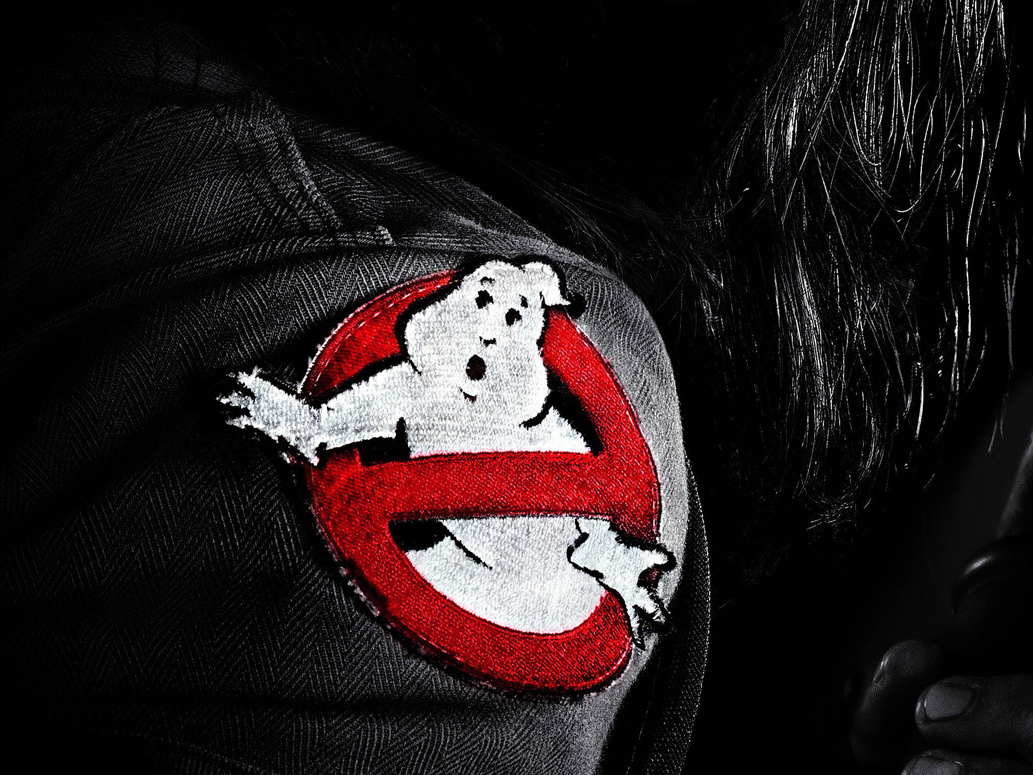 魔鬼剋星 桌布 壁紙 — 近距離拍攝深色牛仔外套上的Ghostbusters標誌布章，黑色頭髮在陰影中。