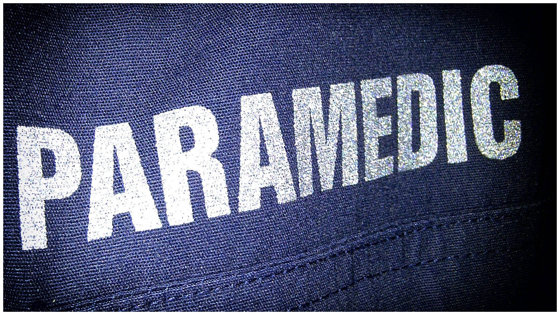 job 桌布 壁紙 — 近距離拍攝深藍色紋理布料上粗體白色閃亮字母「PARAMEDIC」的特寫。