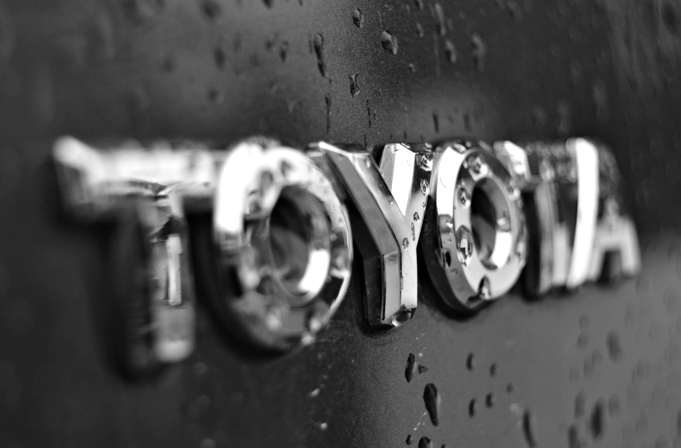 Toyota 桌布 壁紙 — 近距離拍攝濕透的豐田標誌在汽車引擎蓋上，雨滴在單色中閃閃發光。