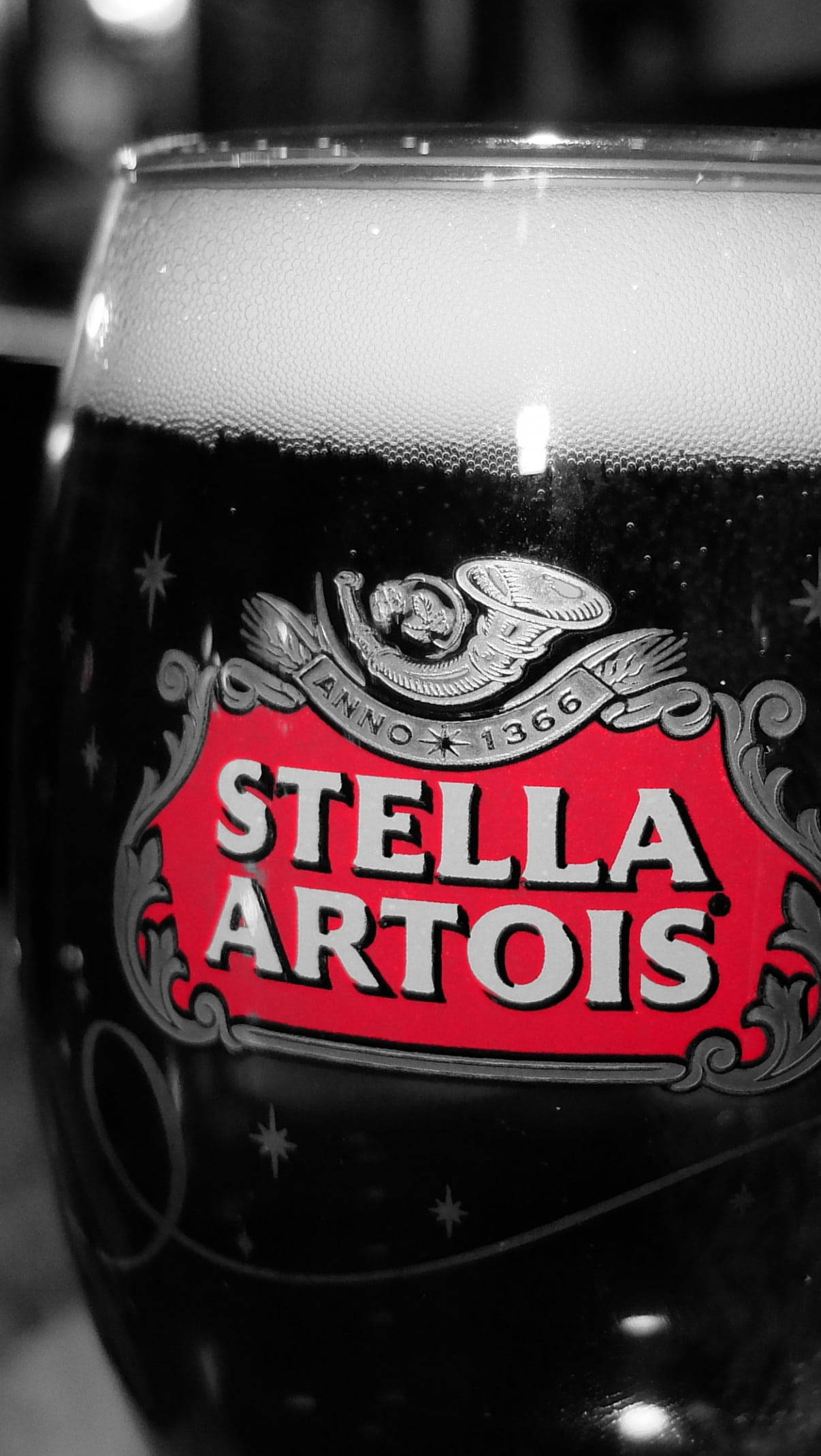 飲料 桌布 壁紙 — 近距離拍攝的Stella Artois啤酒杯，帶有泡沫頭和鮮紅色標誌，背景為黑白。