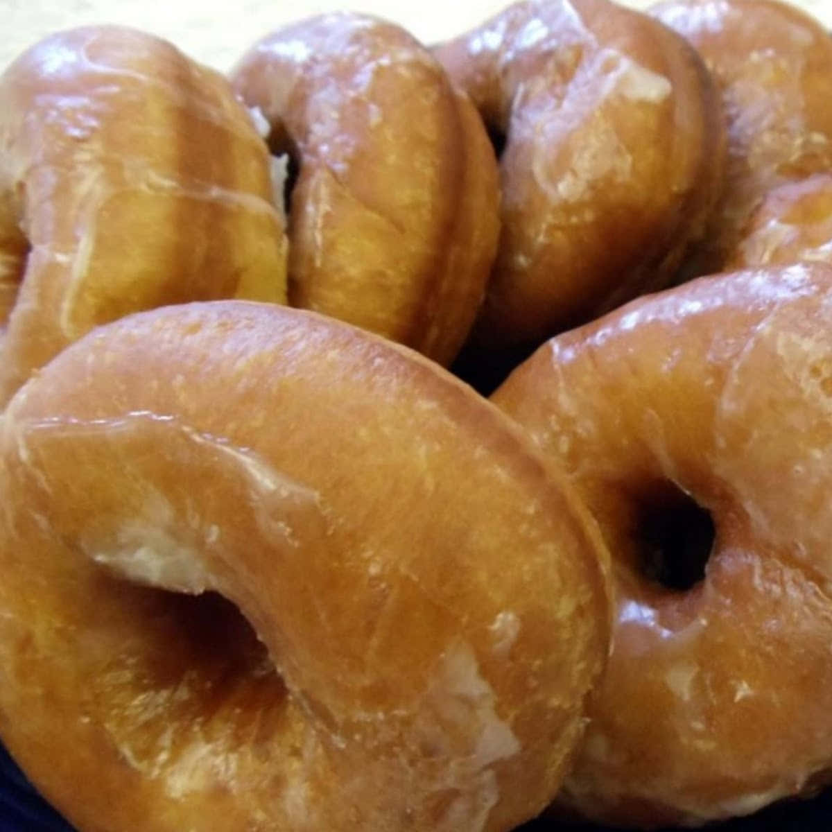 Donut 桌布 壁紙 — 近距離拍攝的亮面釉面甜甜圈堆疊在一起，帶有溫暖的金黃色調和糖光澤。