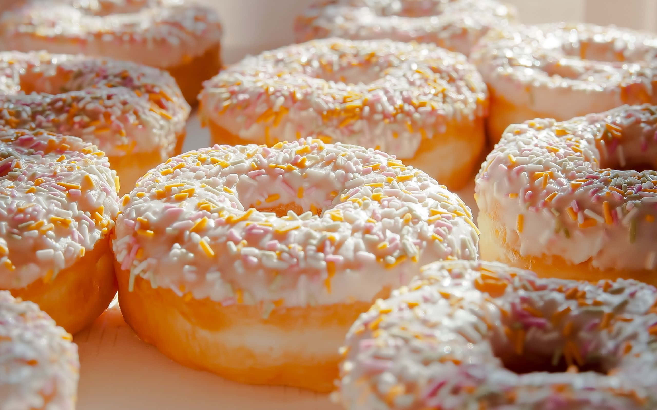 donuts 桌布 壁紙 — 近距離拍攝的糖霜甜甜圈，上面灑滿彩色糖粒，沐浴在溫暖的金色光芒中。