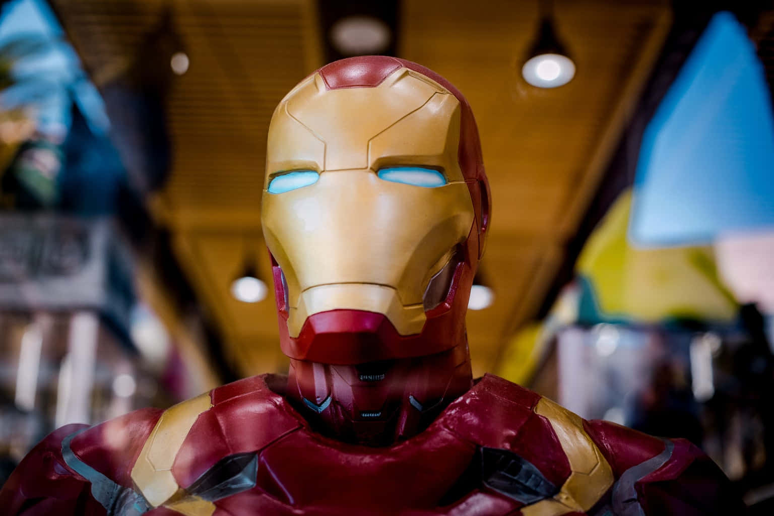 Superhero Movies 桌布 壁紙 — 近距離拍攝的詳細鋼鐵人套裝，帶有發光的藍色眼睛和紅金色盔甲，處於昏暗的室內環境中。