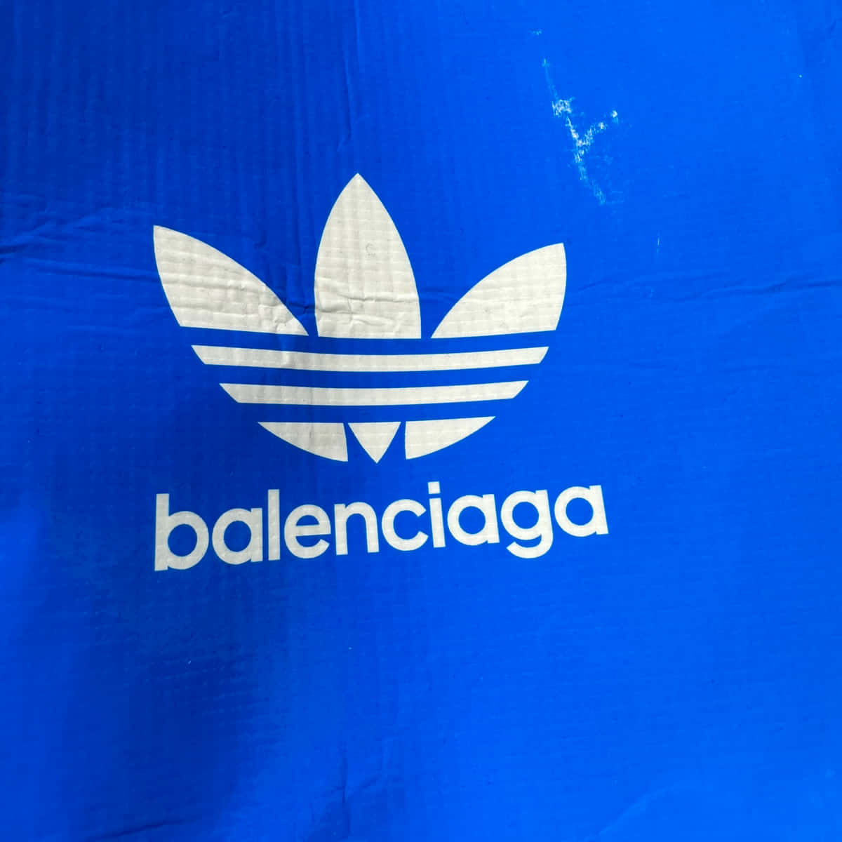巴黎世家 桌布 壁紙 — 近距離拍攝的鮮豔藍色布料，上面印有白色Adidas三葉草標誌和Balenciaga文字。