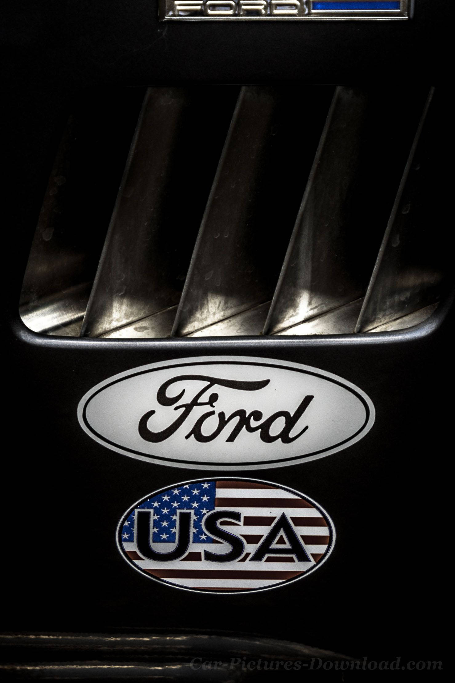 ford iPhone 桌布 壁紙 — 近距離拍攝福特汽車標誌，帶有美國國旗貼紙，位於鍍鉻格柵下方，黑色背景。