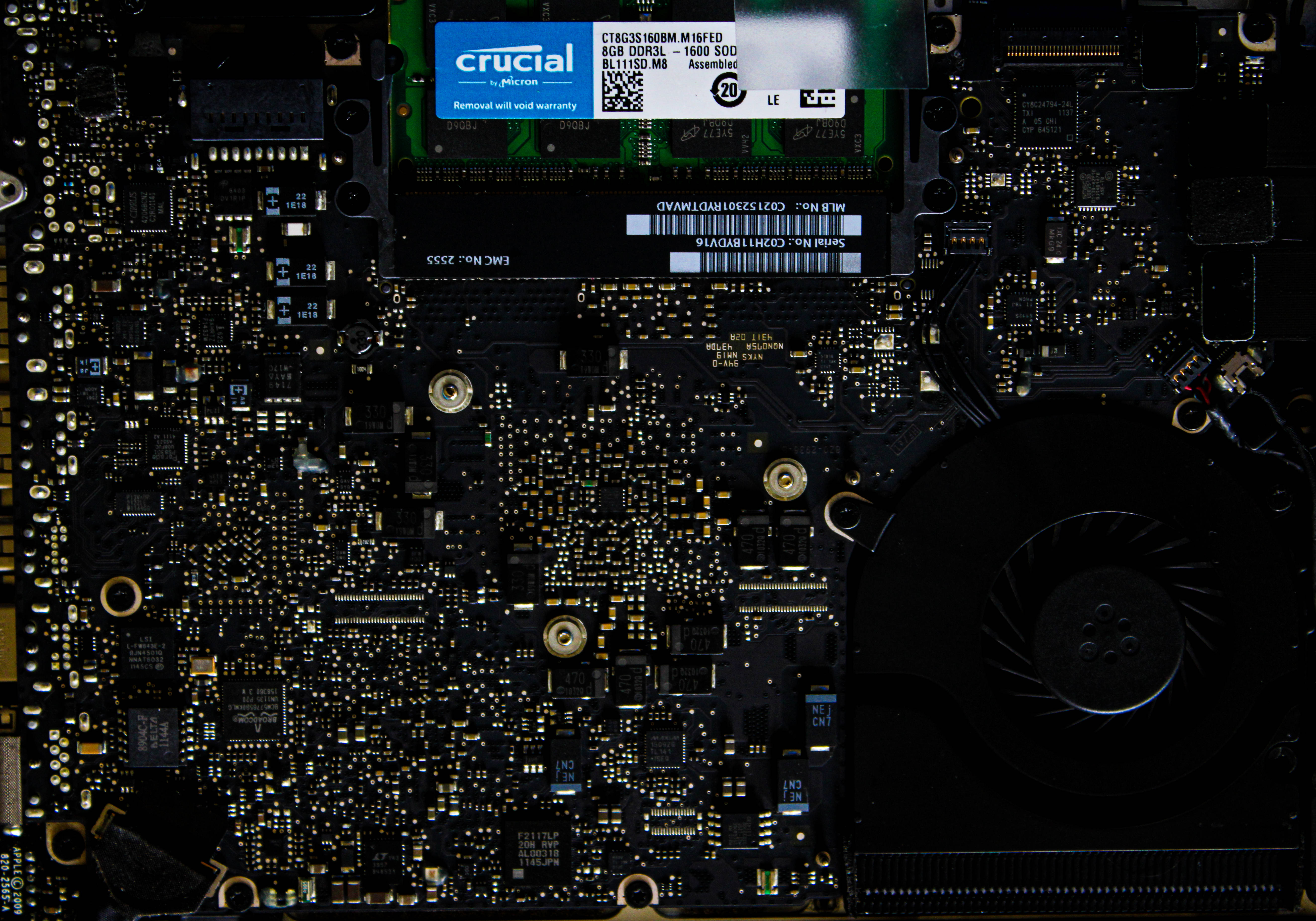 Motherboard 桌布 壁紙 — 近距離拍攝筆記型電腦主機板，在昏暗燈光下帶有發光的金色電路和 Crucial RAM 模組。