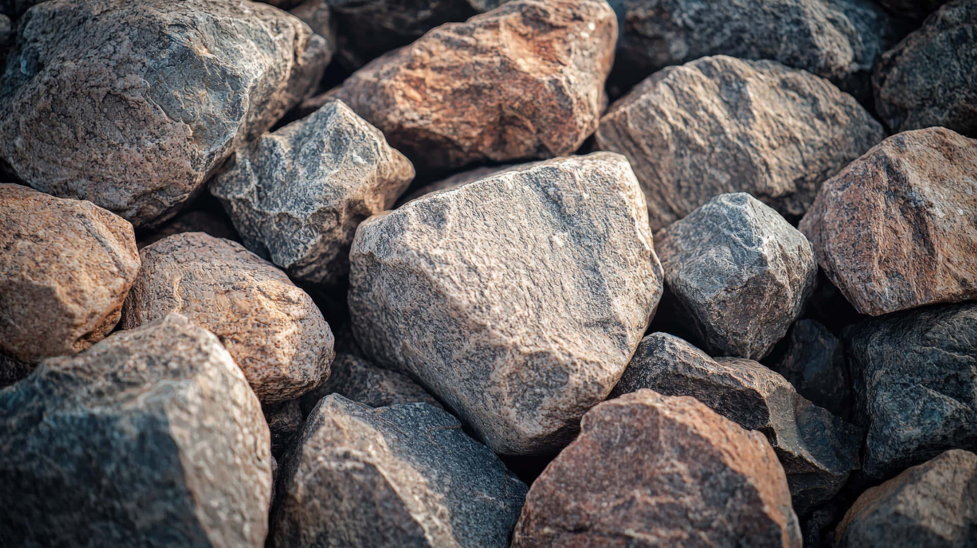 A detailed close-up of various rough, jagged rocks with natural earthy tones 壁紙 — 近距離拍攝粗糙紋理的岩石，以大地色調堆疊，帶有自然陰影。