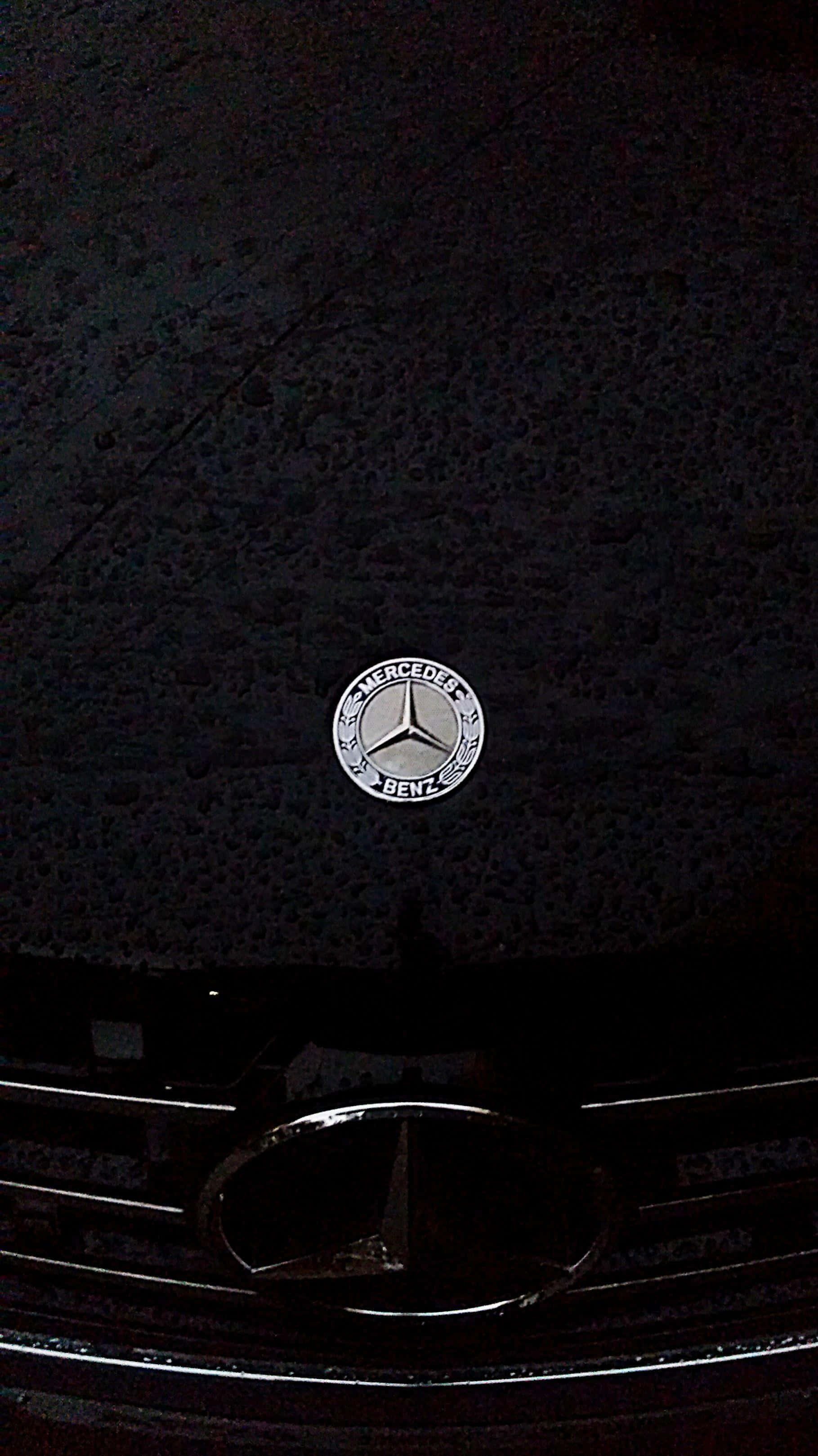 Mercedes Benz Logo 桌布 壁紙 — 近距離拍攝賓士標誌在昏暗燈光下於深色紋理引擎蓋上發光。