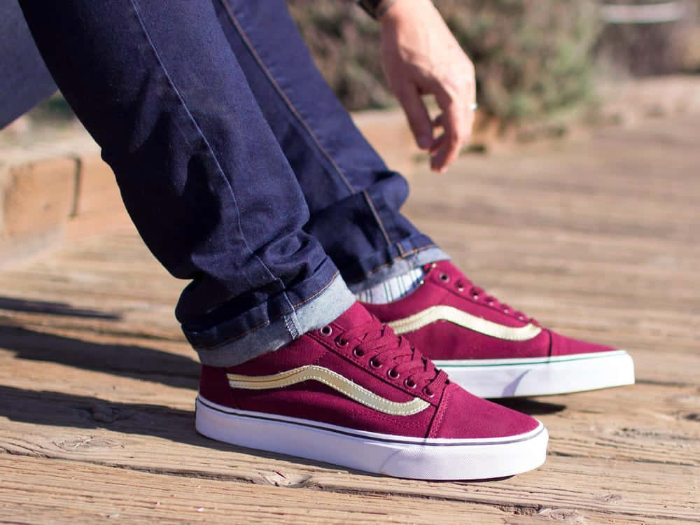 Vans 桌布 壁紙 — 近距離拍攝酒紅色Vans運動鞋，帶金色條紋，置於木甲板上，陽光普照。