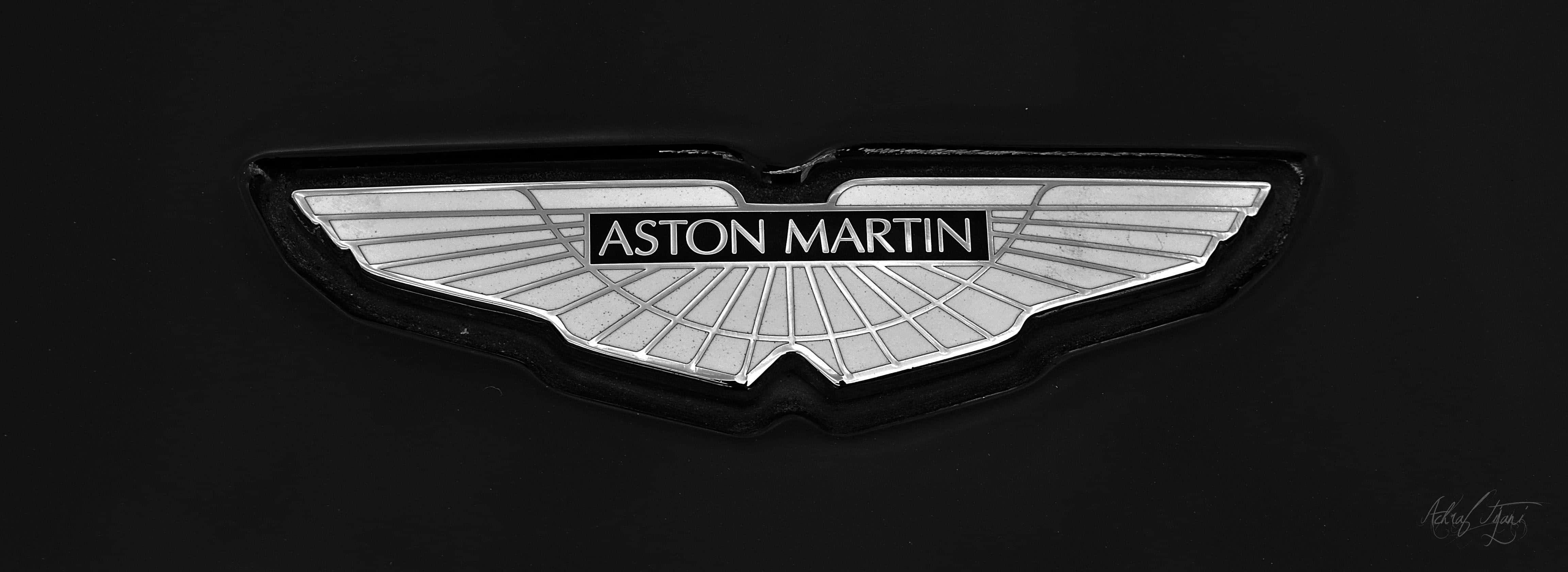 奧斯頓馬丁 桌布 壁紙 — 近距離拍攝銀色Aston Martin翼形標誌徽章在啞光黑色汽車表面上閃耀。