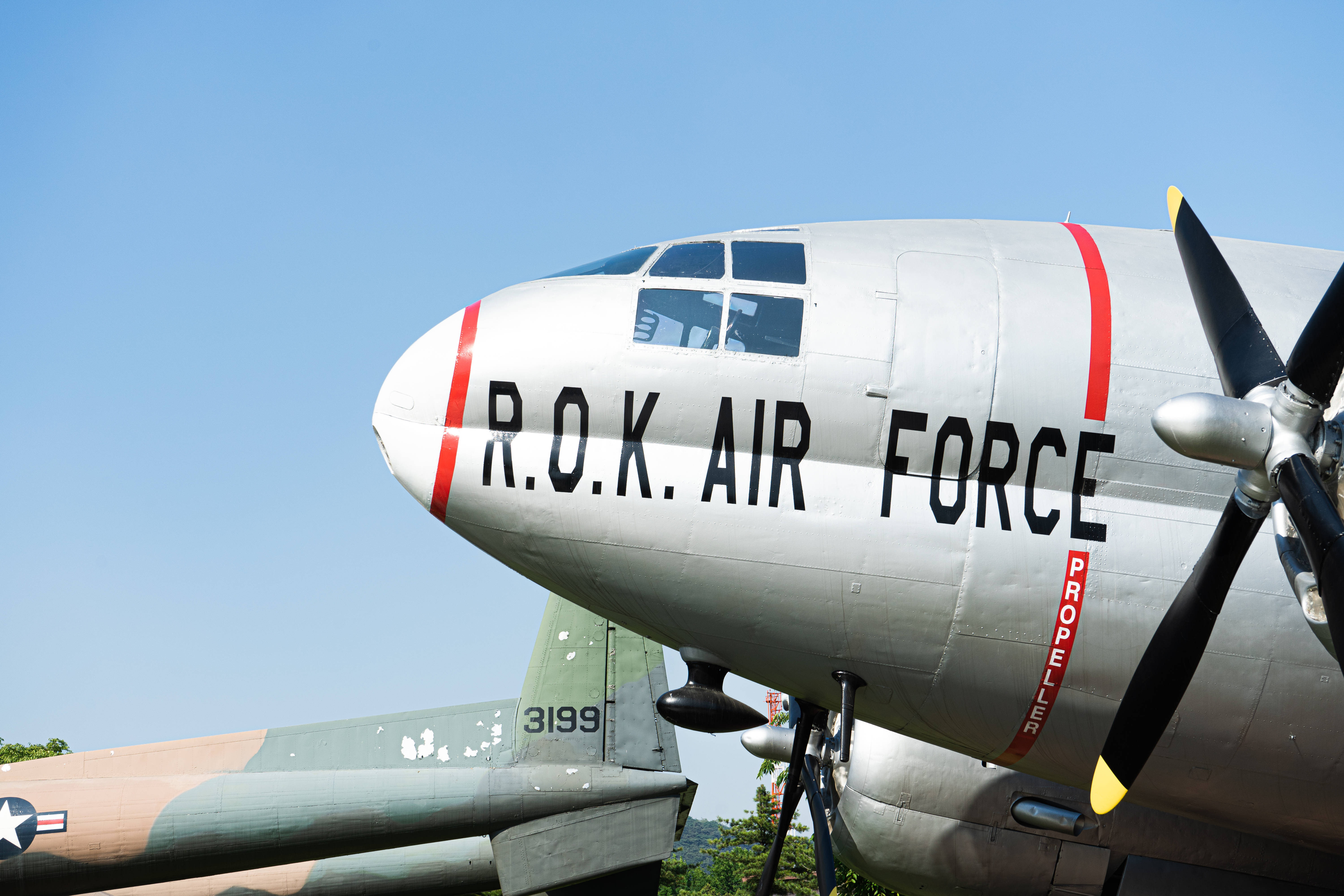 軍事動圖 桌布 壁紙 — 近距離拍攝銀色大韓民國空軍螺旋槳飛機，背景為晴朗藍天及另一架飛機。