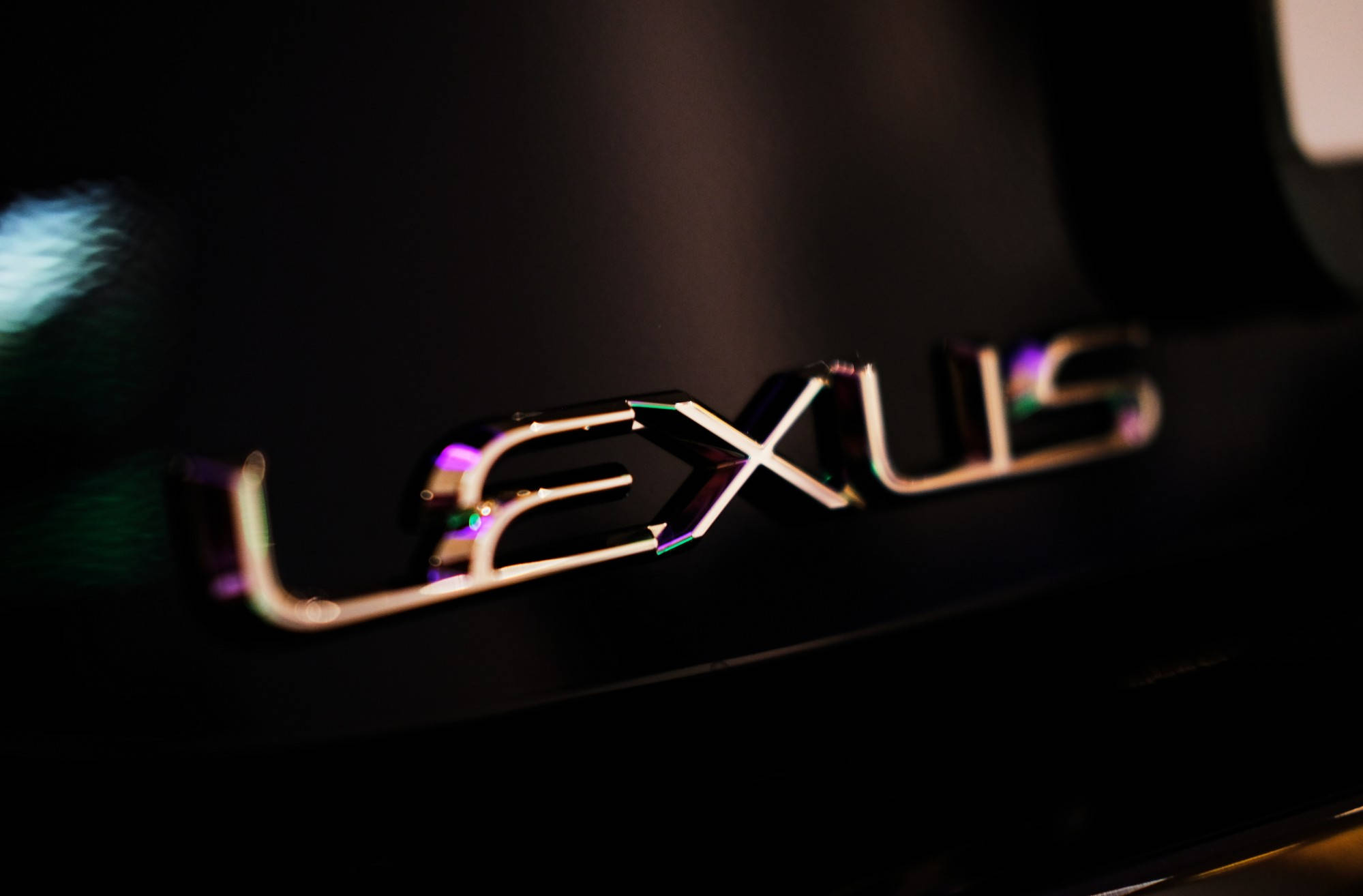 Lexus 標誌 桌布 壁紙 — 近距離拍攝閃亮的 Lexus 標誌，在黑暗背景下反射出彩虹色調。