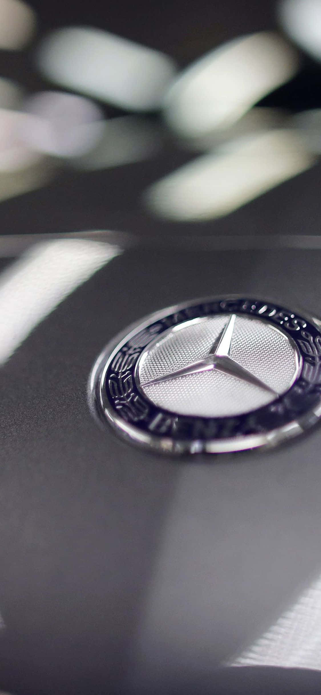 桌布 壁紙 — 近距離拍攝閃亮的 Mercedes-Benz 標誌，位於時尚黑色引擎蓋上，背景柔和散景。